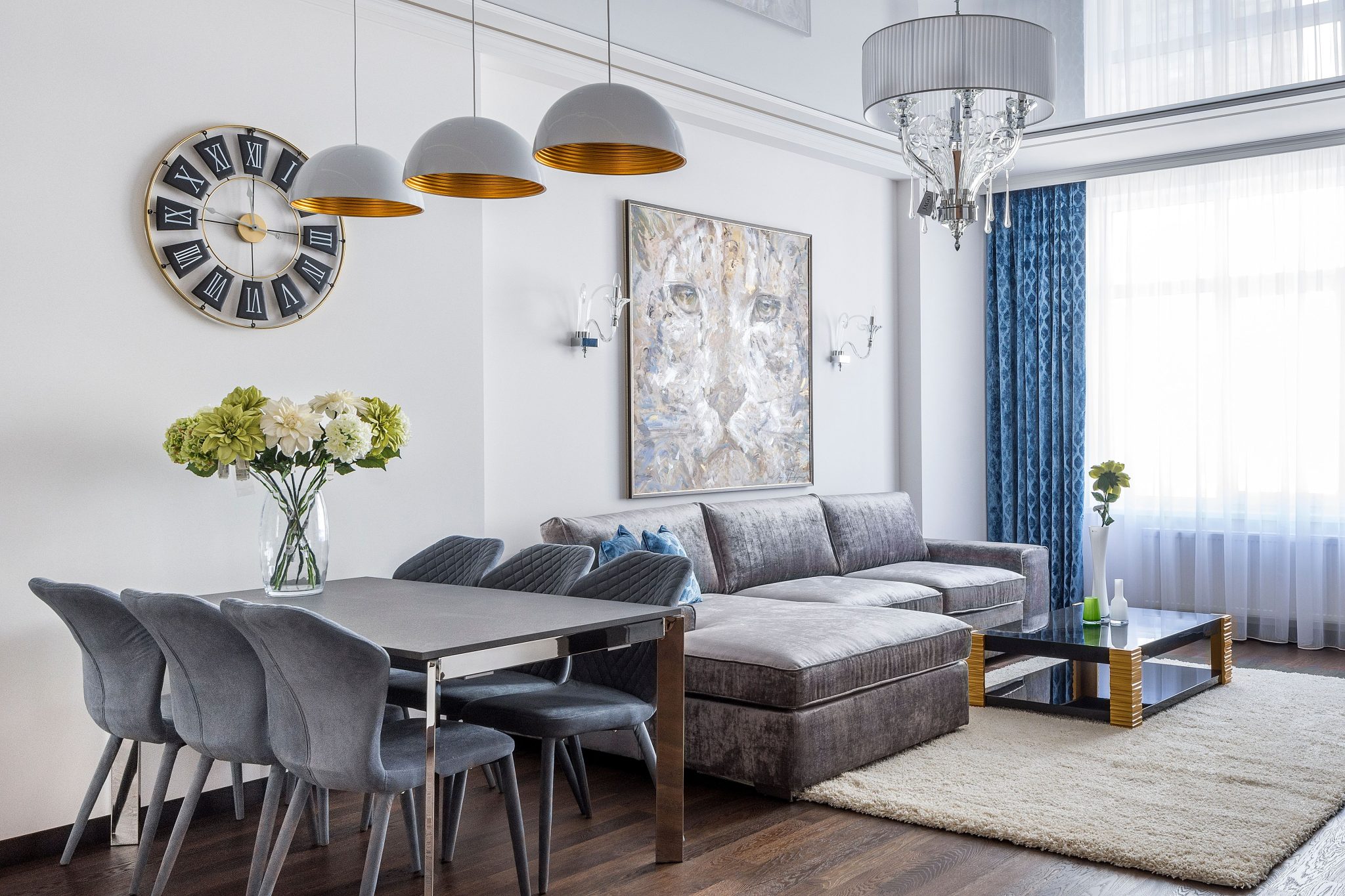 Interior design of stylish cozy living room with comfortable sofa and table with chairs in dining zone decorated with picture and flowers in vase