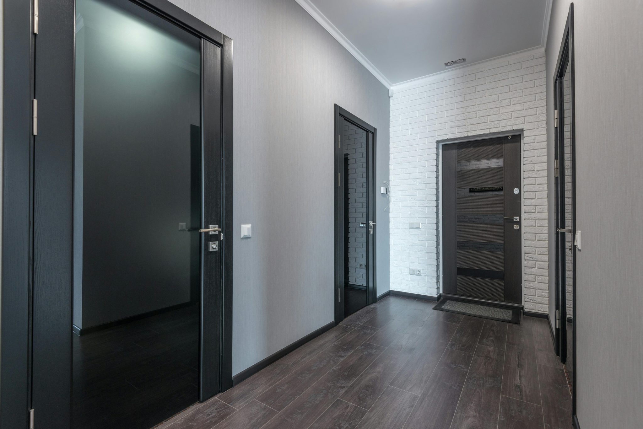 Interior of empty spacious corridor with laminate floor and black doors with glass parts and white ceiling and gray painted walls