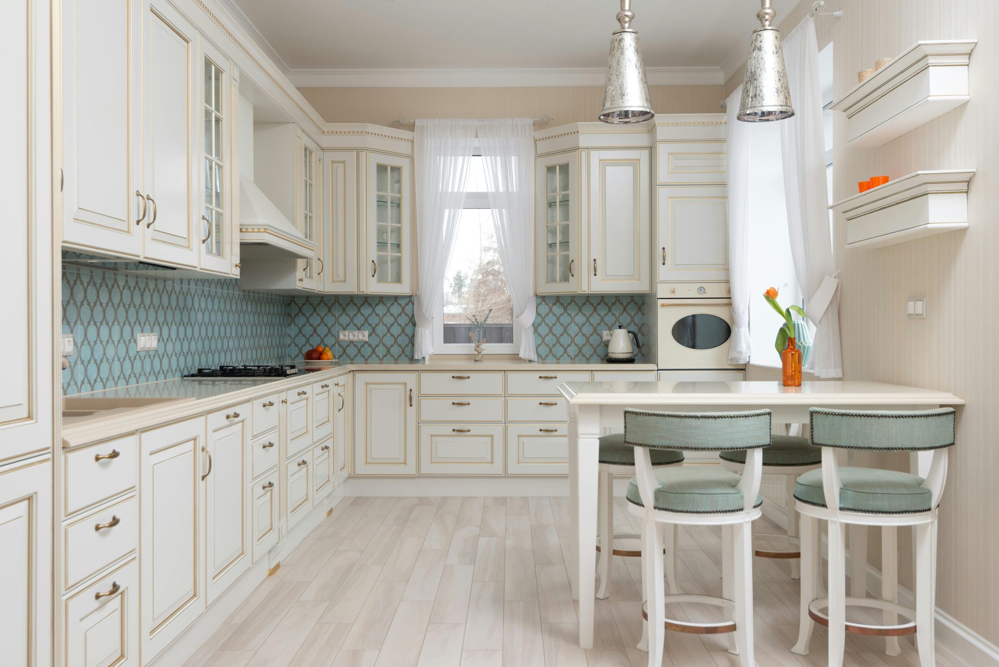 Interior of light classic kitchen with white ornamental cabinets near wooden table and chairs next to window with curtains
