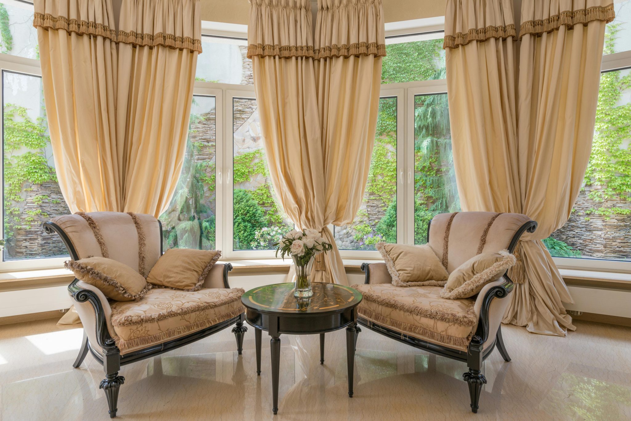 Interior of luxurious living room with table decorated with vase with flowers near armchairs and windows with beige curtains