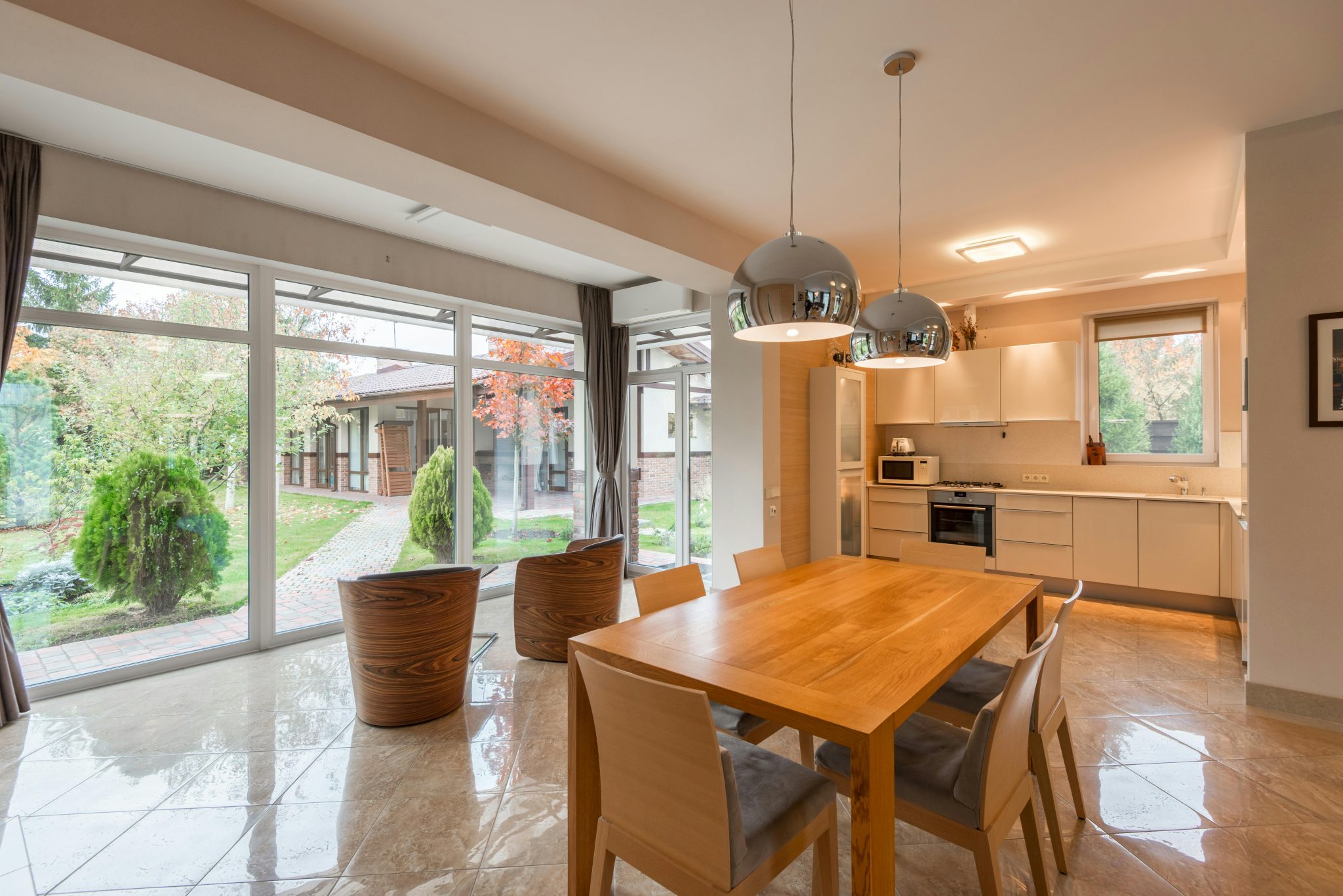 Interior of modern cottage made in minimalist style with wooden furniture in dining zone and convenient kitchen with built in appliances