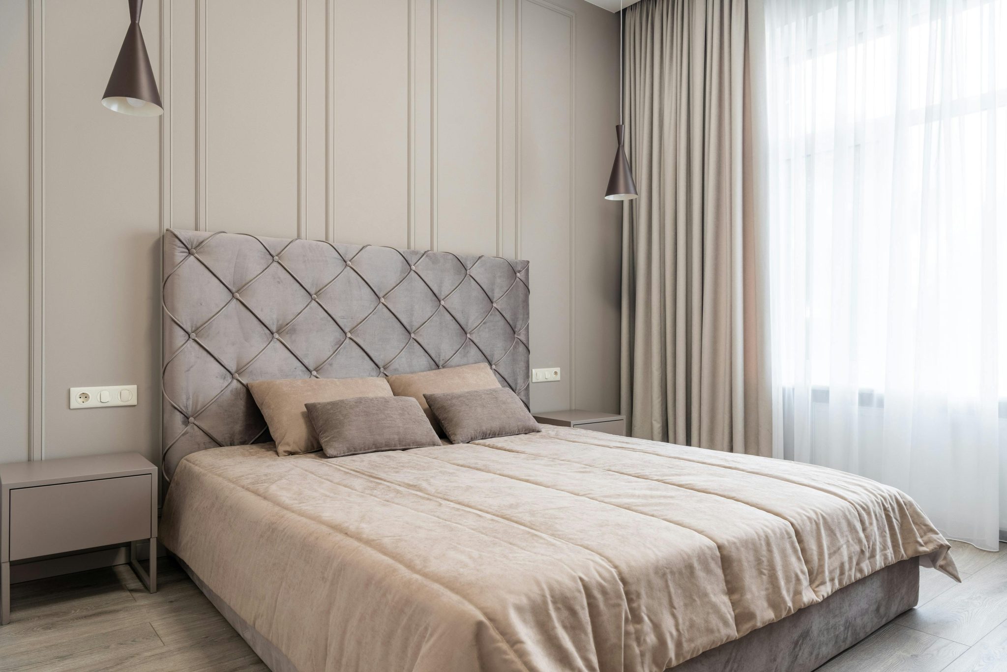 Interior of modern light bedroom with pillows on bed near tables under lamps and windows with curtains
