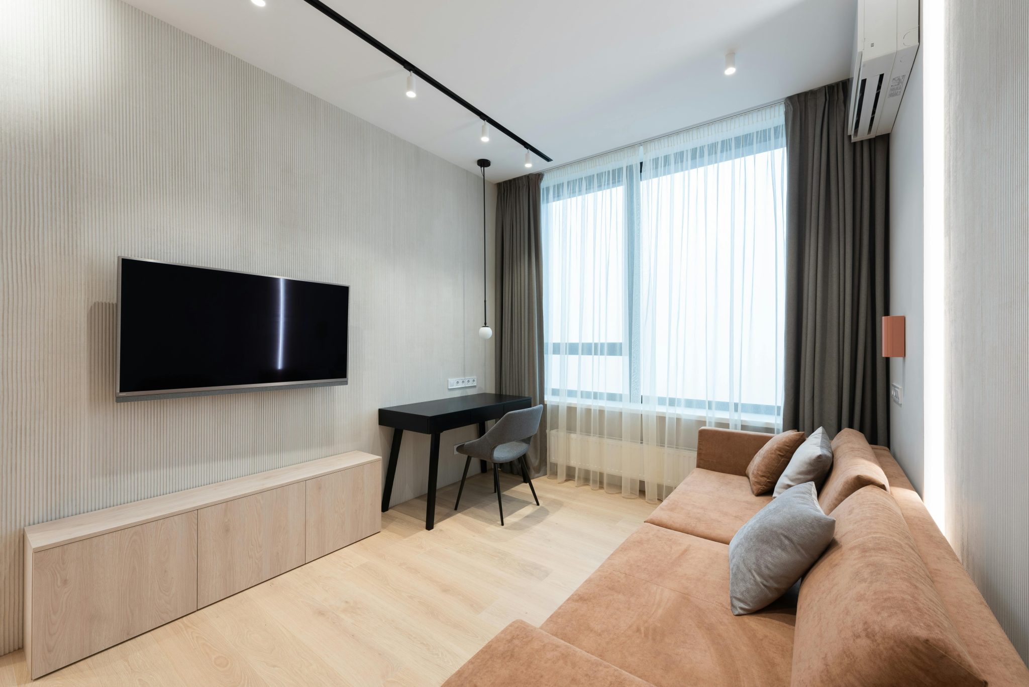 Interior of modern living room with sofa with pillows and TV on wall next to table with chair and curtains on window