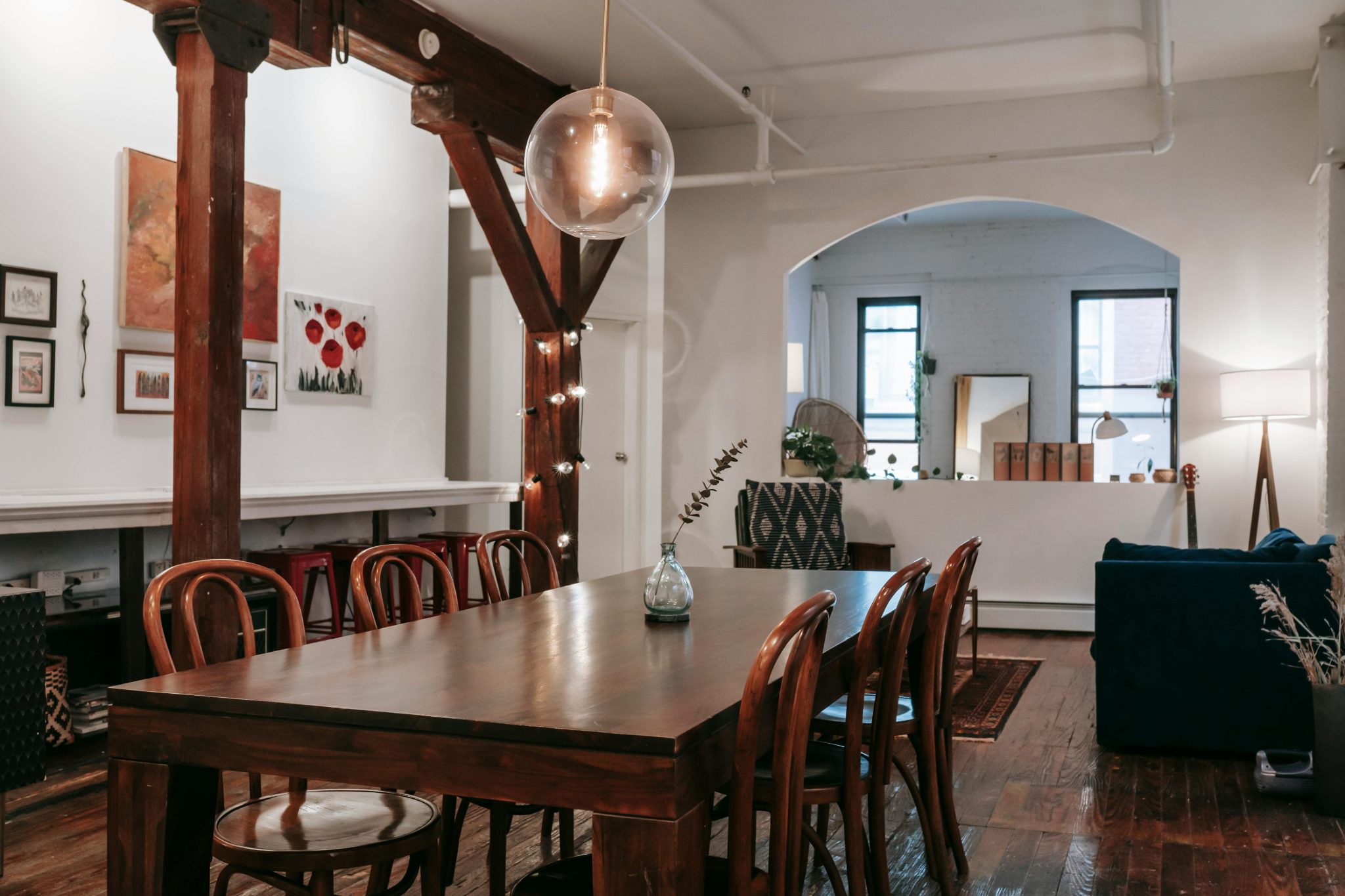 Interior of wooden table with glowing lamps hanging on pillar in creative light living room with furniture and arched aperture