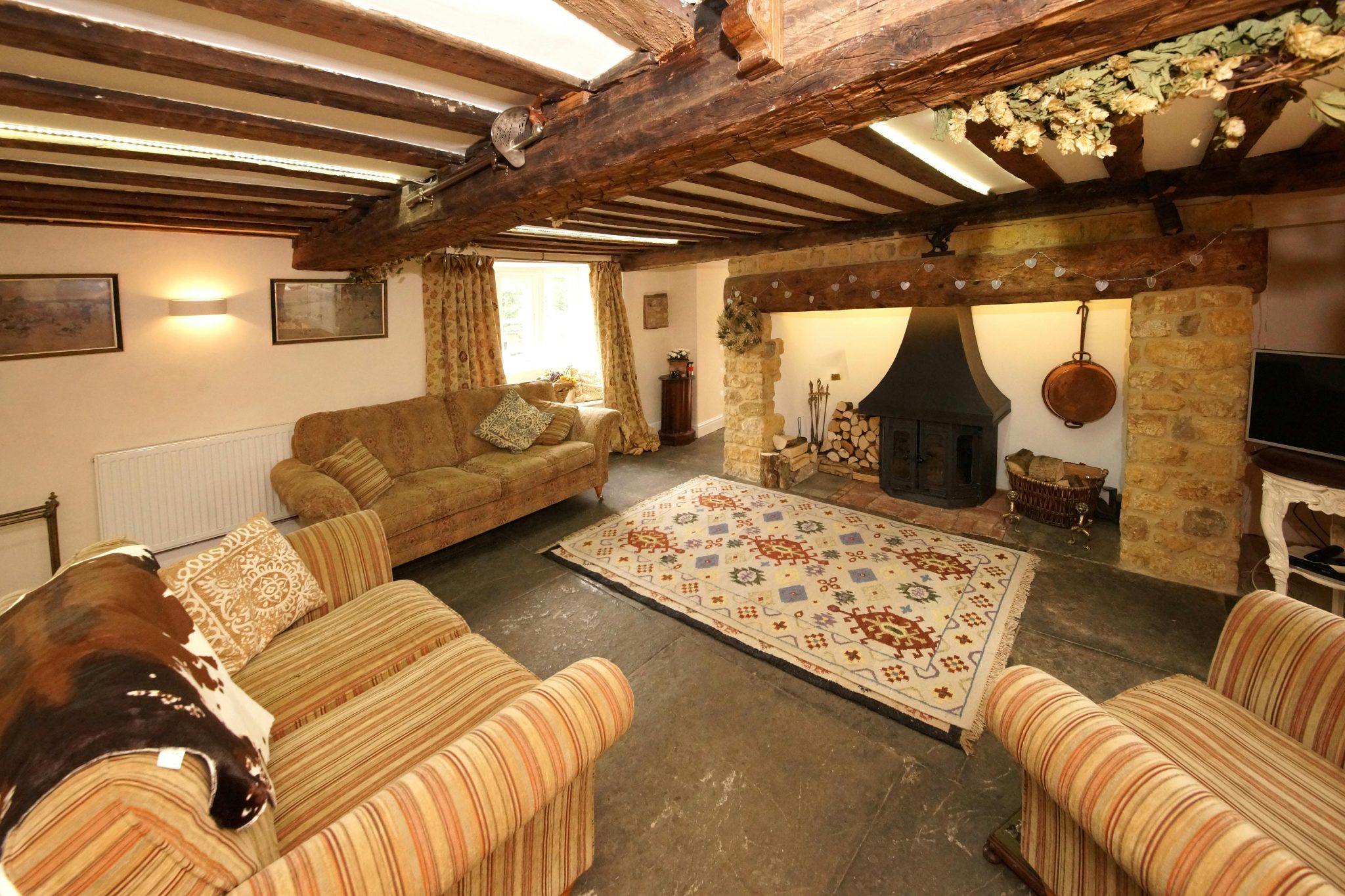 Inviting living room with rustic decor features exposed beams, patterned rug, and a traditional fireplace.