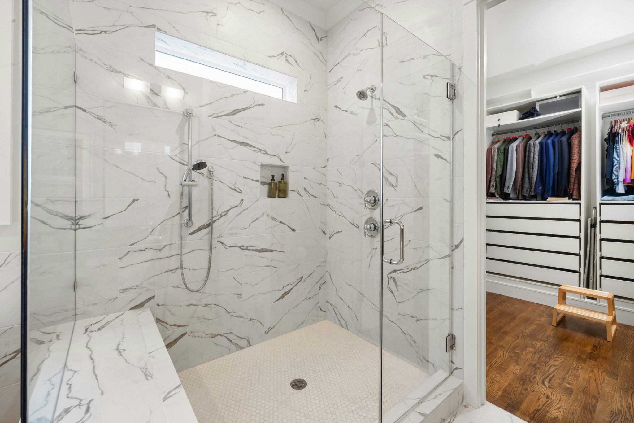 Luxurious marble shower design with glass doors, adjacent to an organized walk-in closet.
