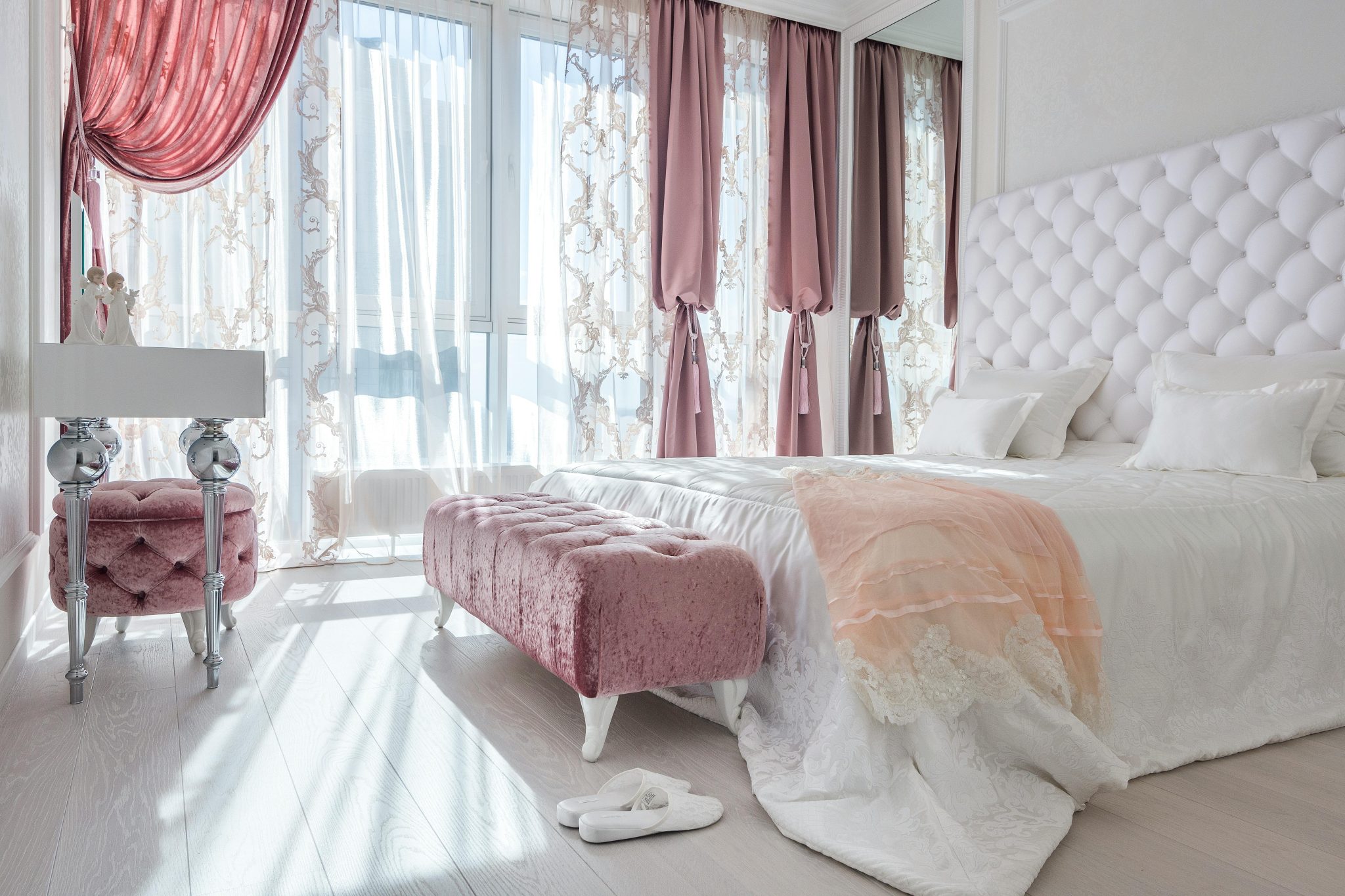 Luxury interior of white and rosy bedroom with big bed soft ottomans and elegant decor