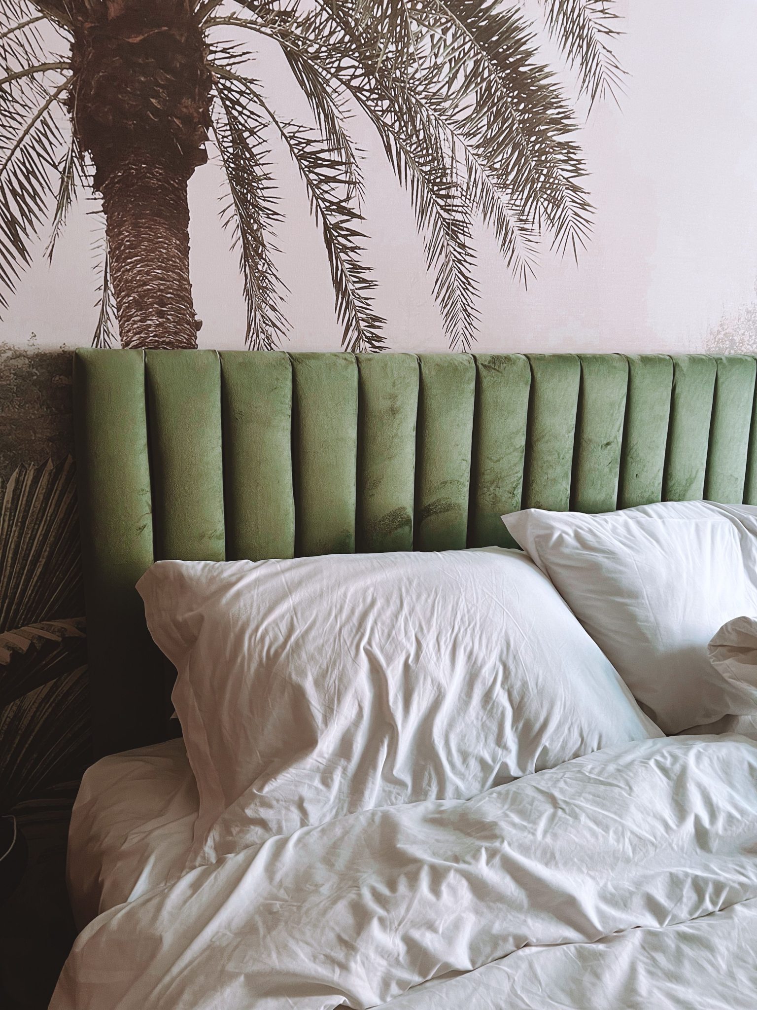 Modern bedroom design with a green headboard and tropical wallpaper.