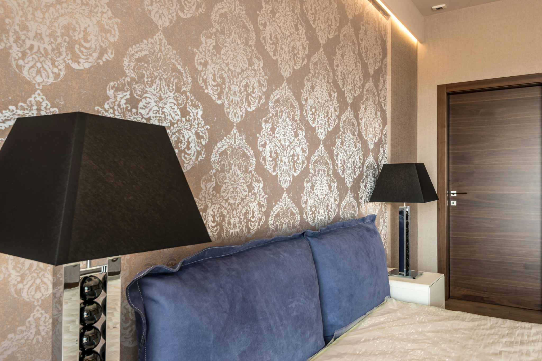 Modern bedroom with elegant wallpaper design, blue pillows, and stylish black lamps.