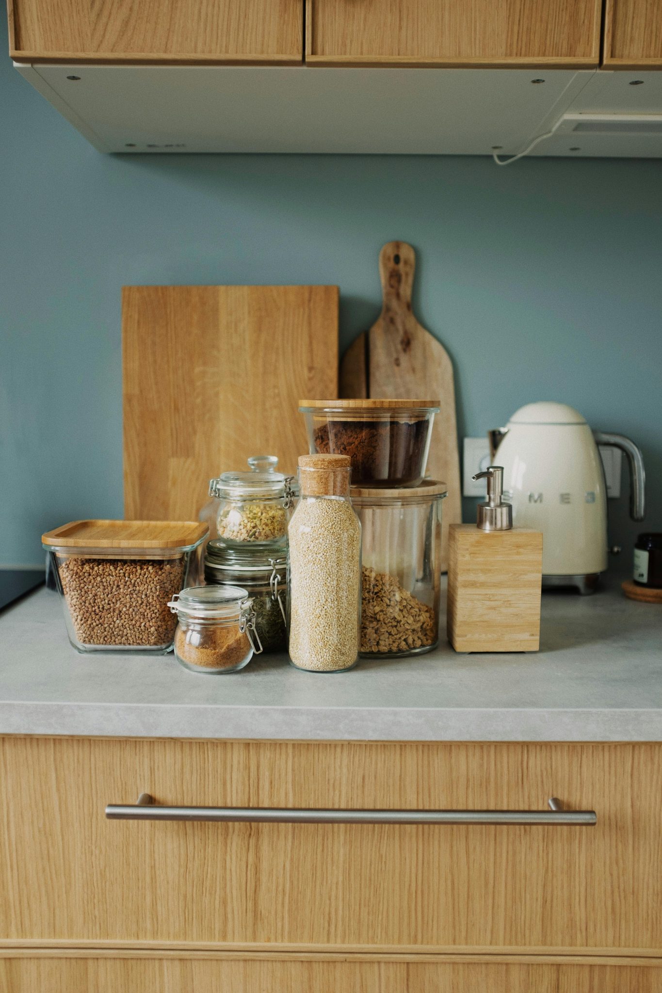 Modern kitchen setup featuring glass jars, wooden board, and an electric kettle on a counter.