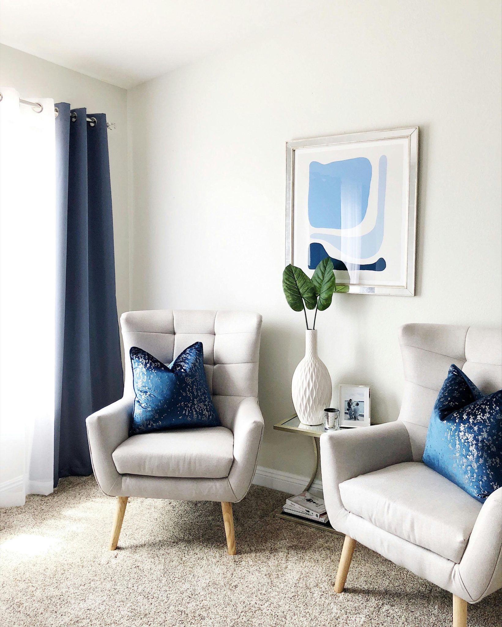 Modern living room with two chairs, blue pillows, and abstract art.