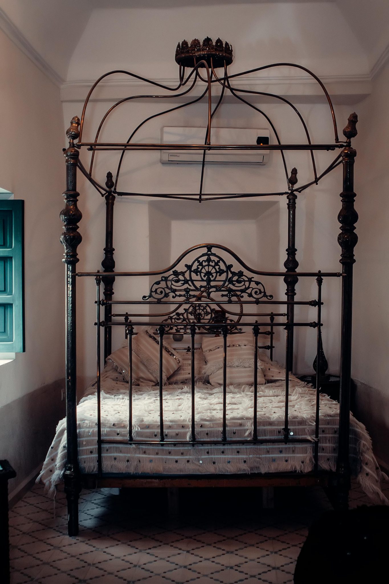 Ornate wrought iron bed in a Moroccan riad with traditional decor and bedding.