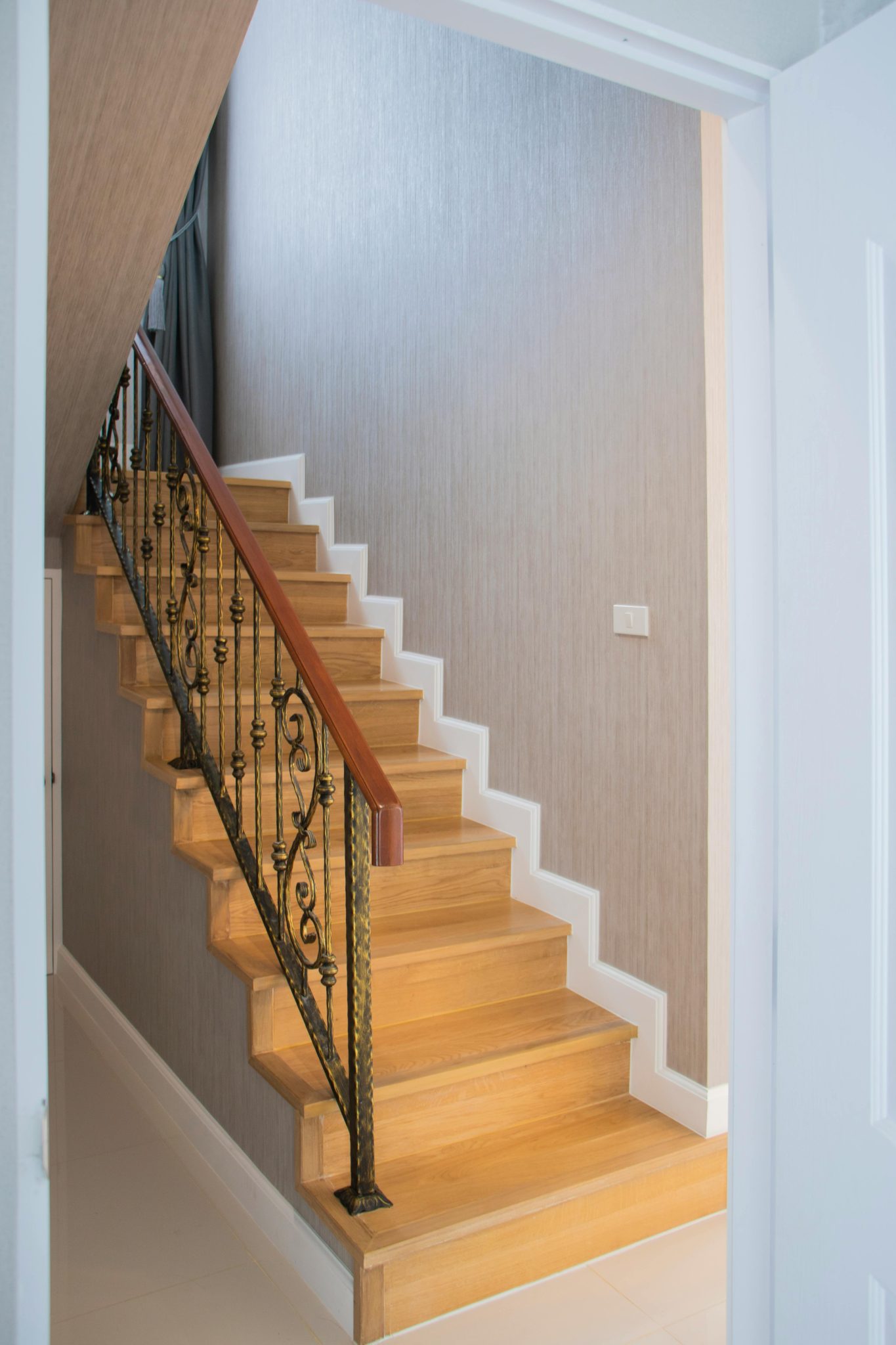 Sleek wooden staircase with an ornate iron railing in a modern home interior.