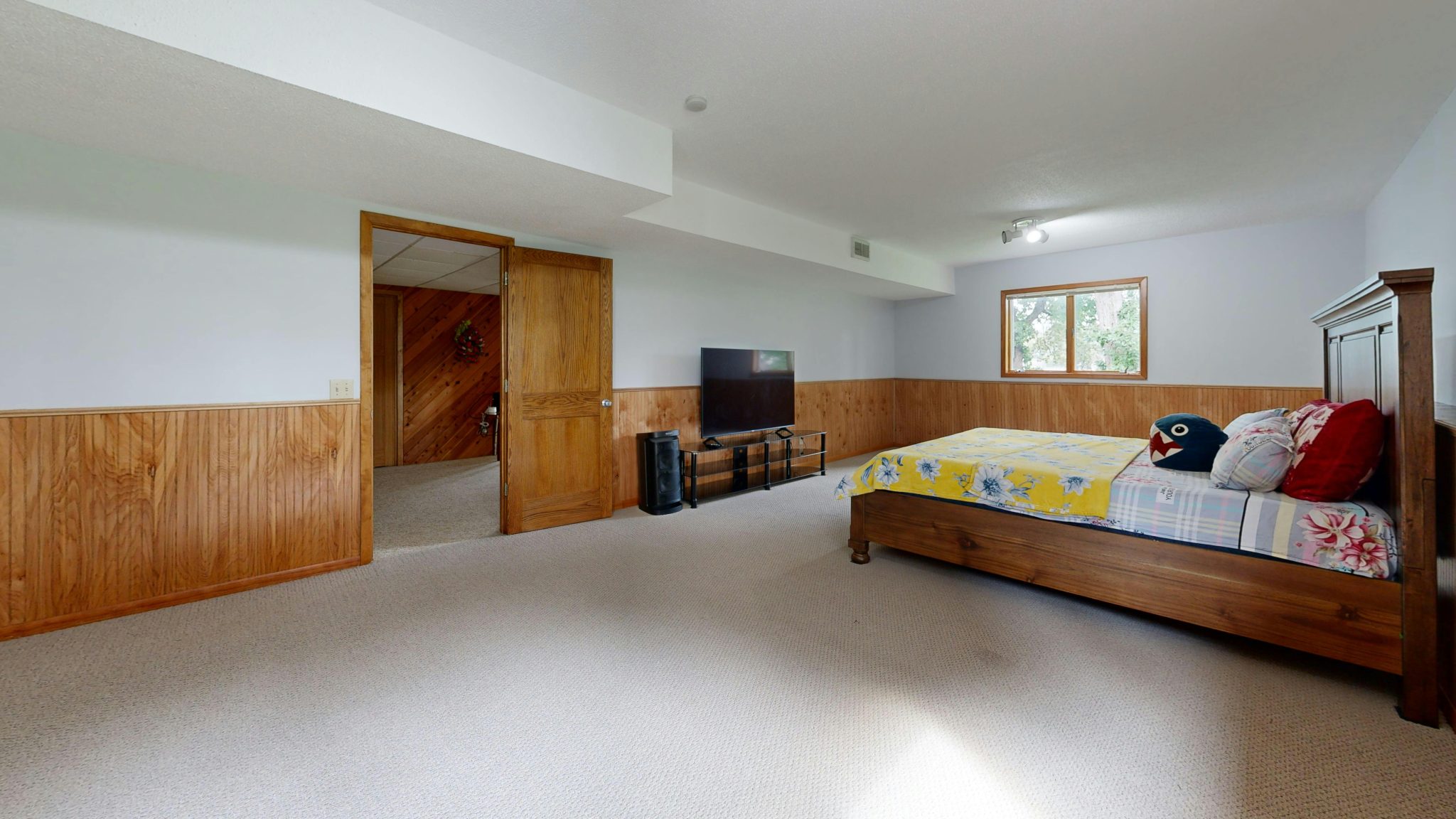 Spacious basement bedroom with wooden decor and modern TV setup.