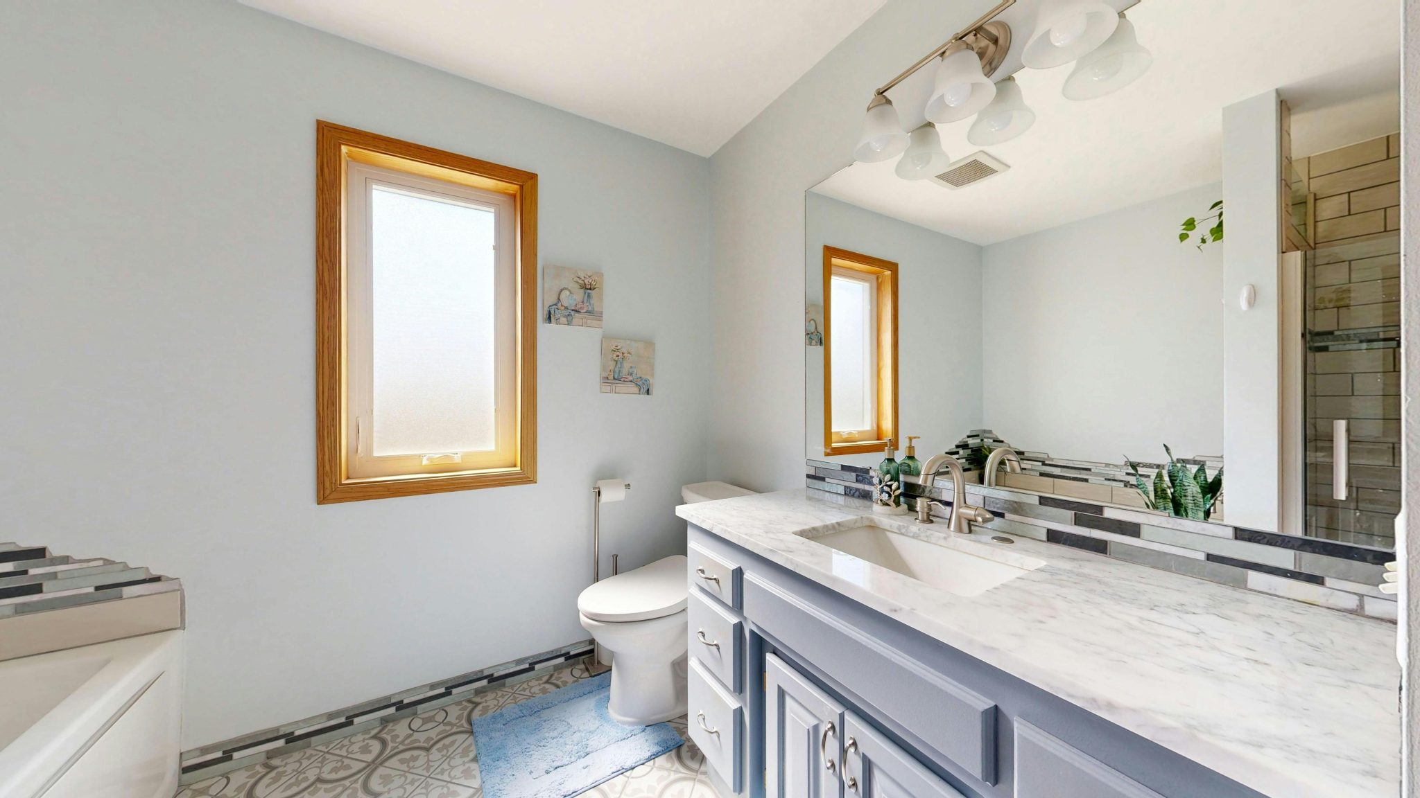 Spacious bathroom featuring a marble vanity, large mirror, and bright lighting.