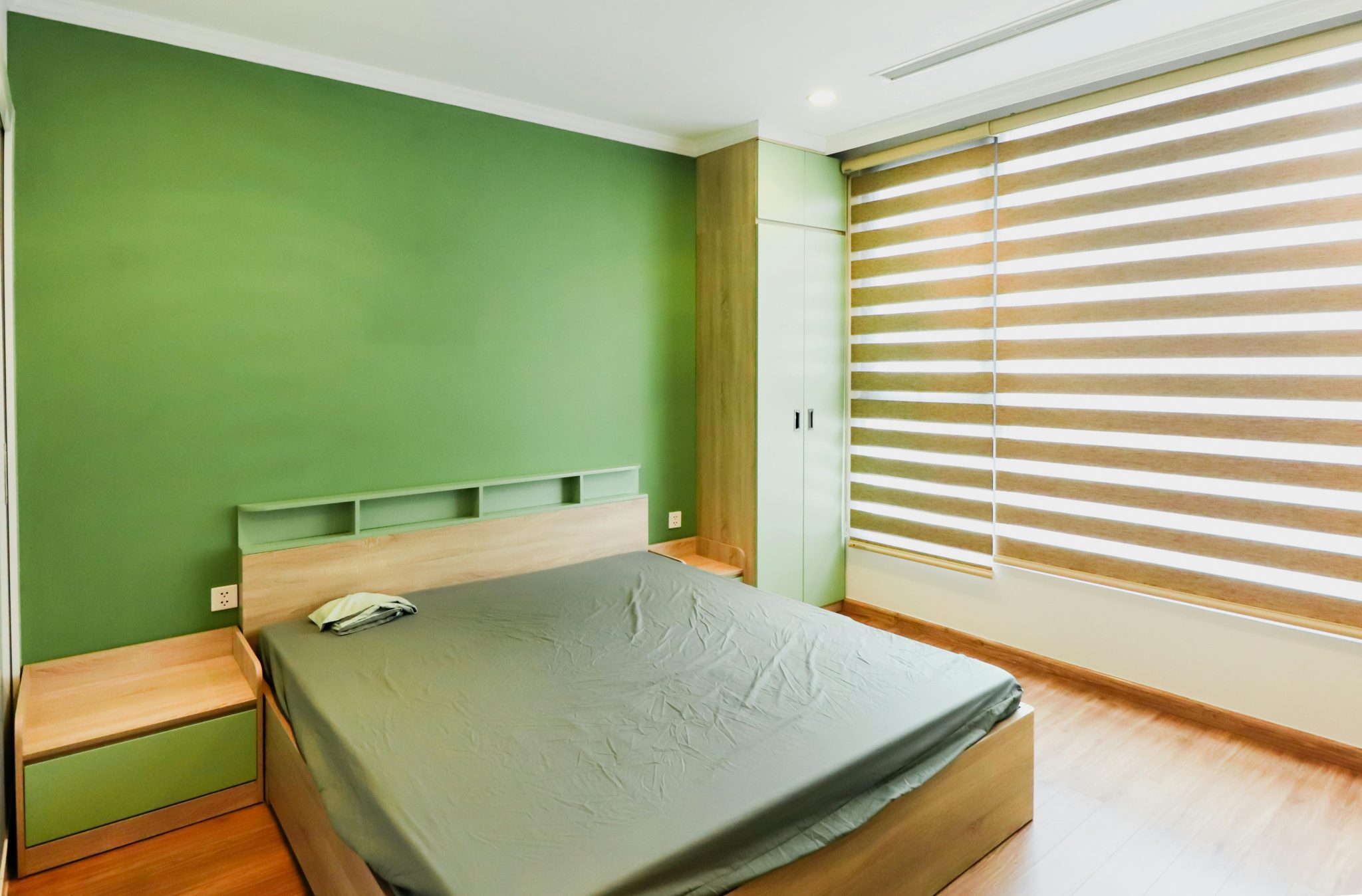 Spacious bedroom featuring a green accent wall, minimalistic furniture, and striped blinds.