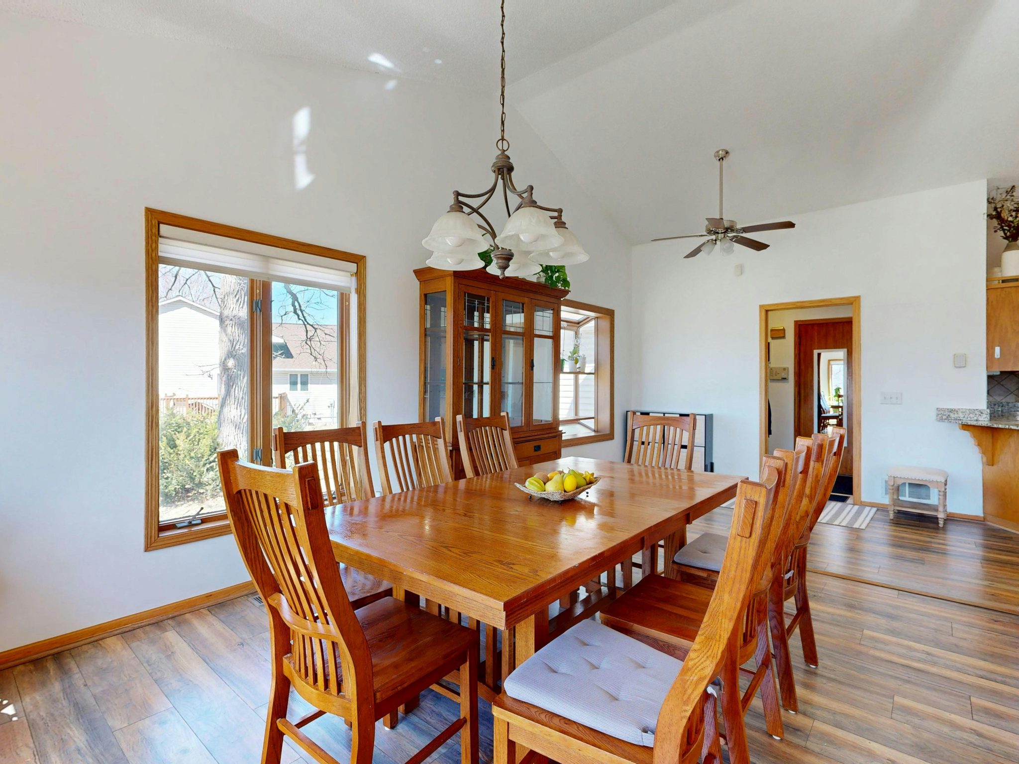 Spacious dining room featuring a wooden table set, ceiling fan, and natural light from a large window.