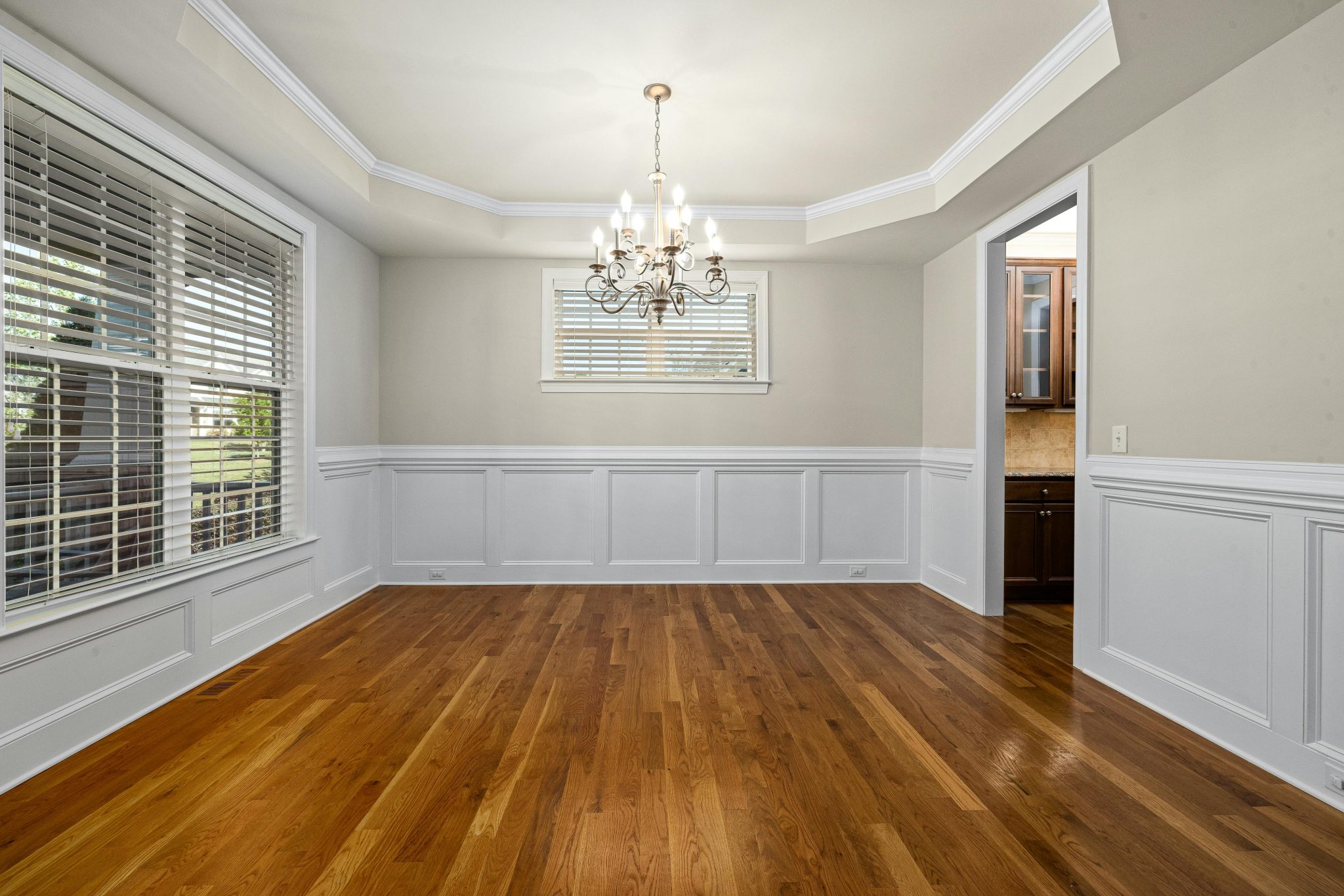 Spacious empty dining room featuring a classic chandelier and wooden flooring.