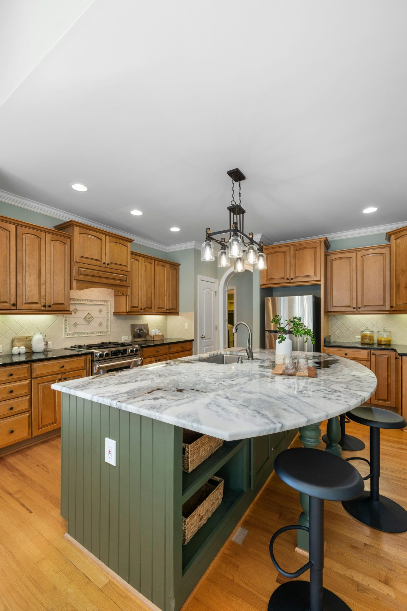 Spacious kitchen with marble island, wooden cabinetry, and elegant lighting for a modern cooking space.