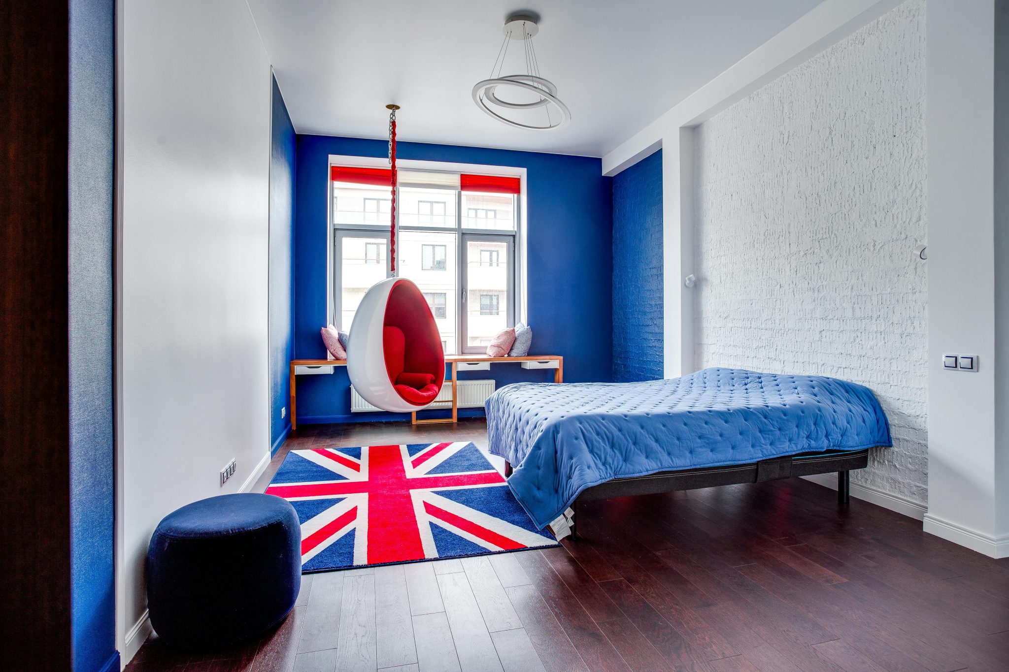 Stylish bedroom featuring a Union Jack rug, blue bedspread, and egg chair, perfect blend of comfort and design.