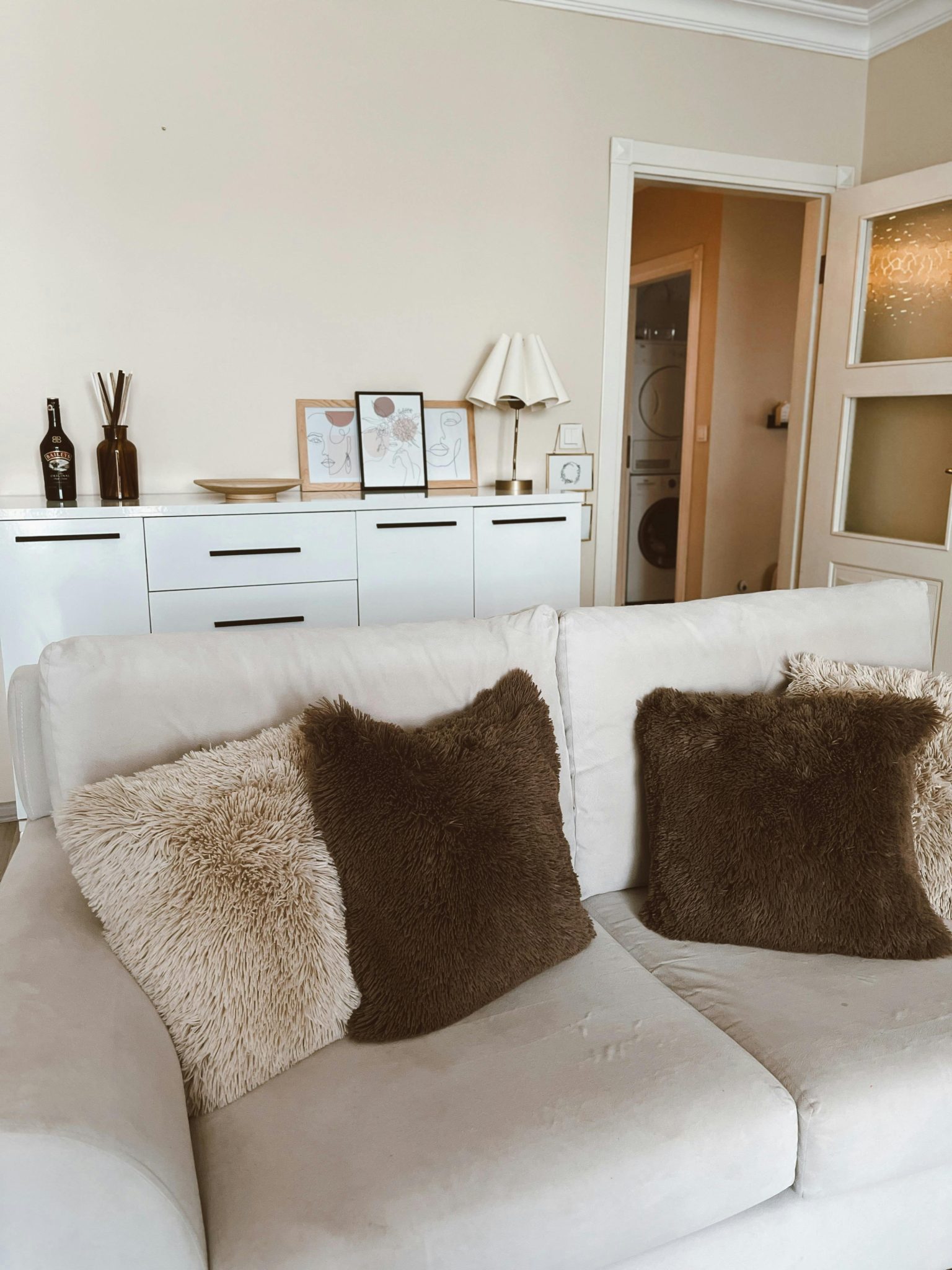 Stylish beige living room with plush pillows and modern decor.