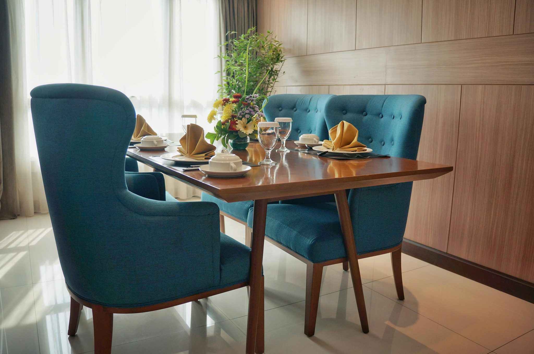 Stylish dining room with blue chairs set for an elegant meal, featuring floral centerpiece.