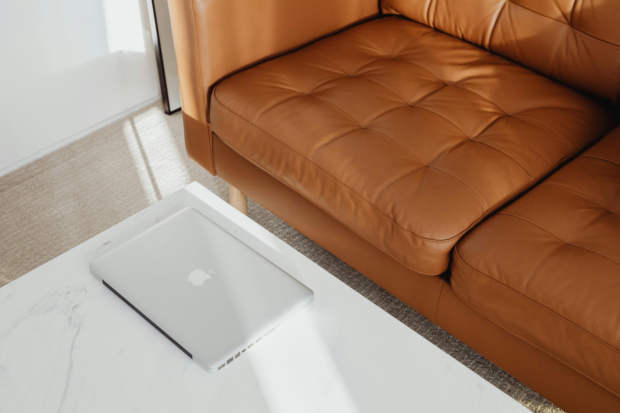 Stylish living room featuring a brown leather couch and laptop on a marble table.