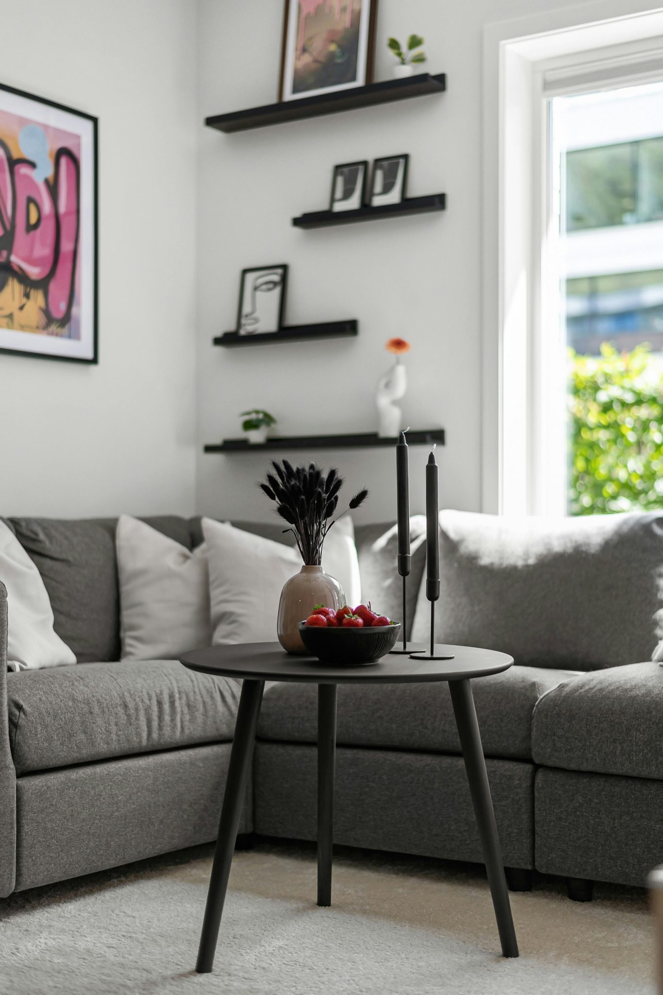 Stylish living room featuring a grey couch, table, and decorative shelves with natural light.