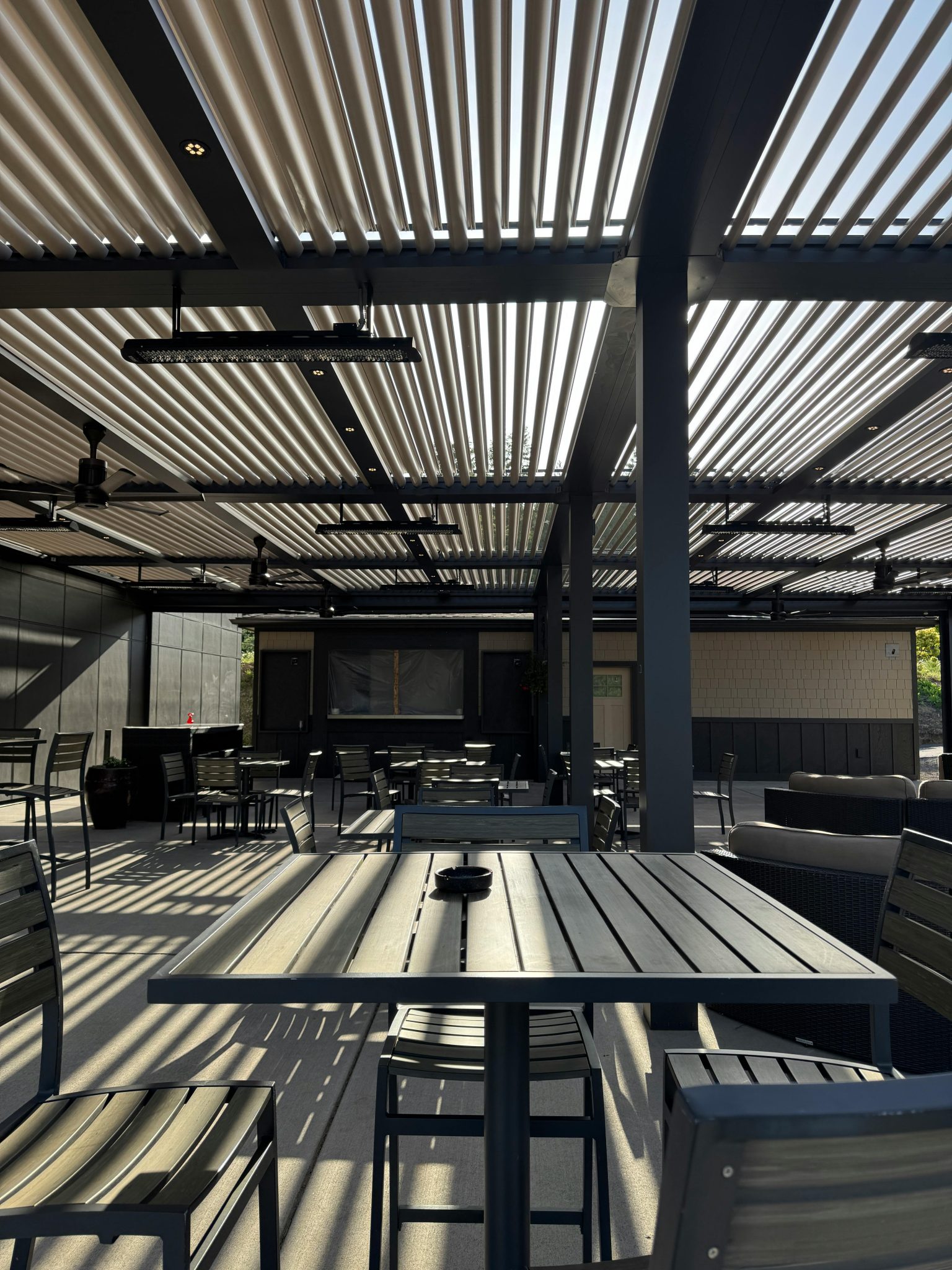 Stylish outdoor patio area with metal furniture and slatted pergola roof casting shadows, ideal for leisure.
