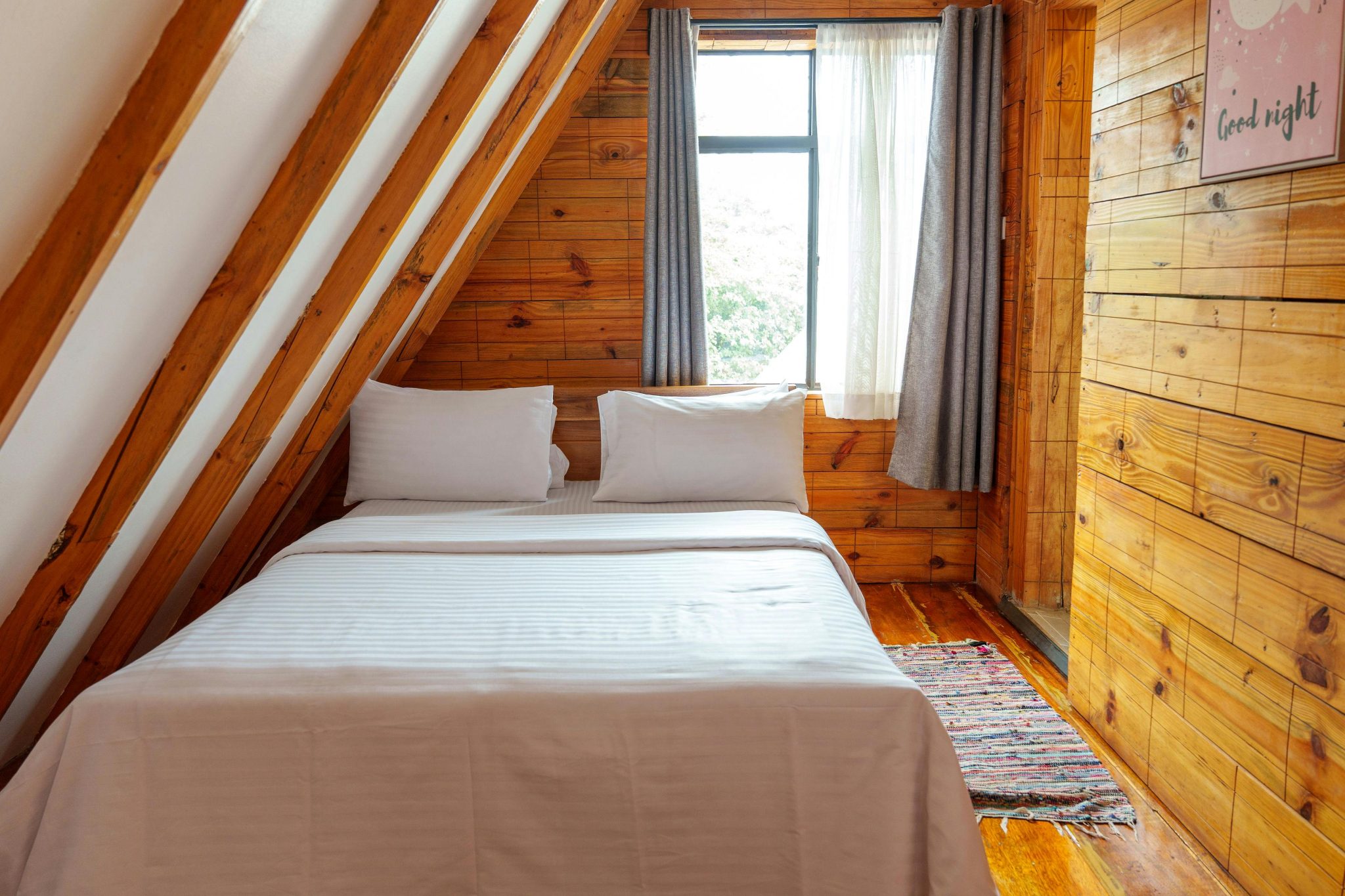 Warm and inviting A-frame cabin bedroom featuring wooden walls, white bedding, and natural light.