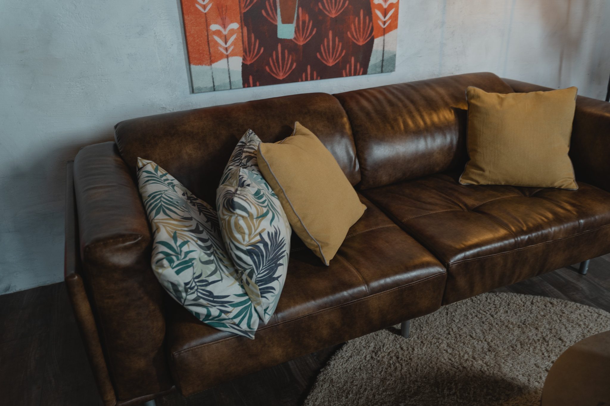 Warm brown leather sofa with patterned and plain pillows in a cozy living room setting.
