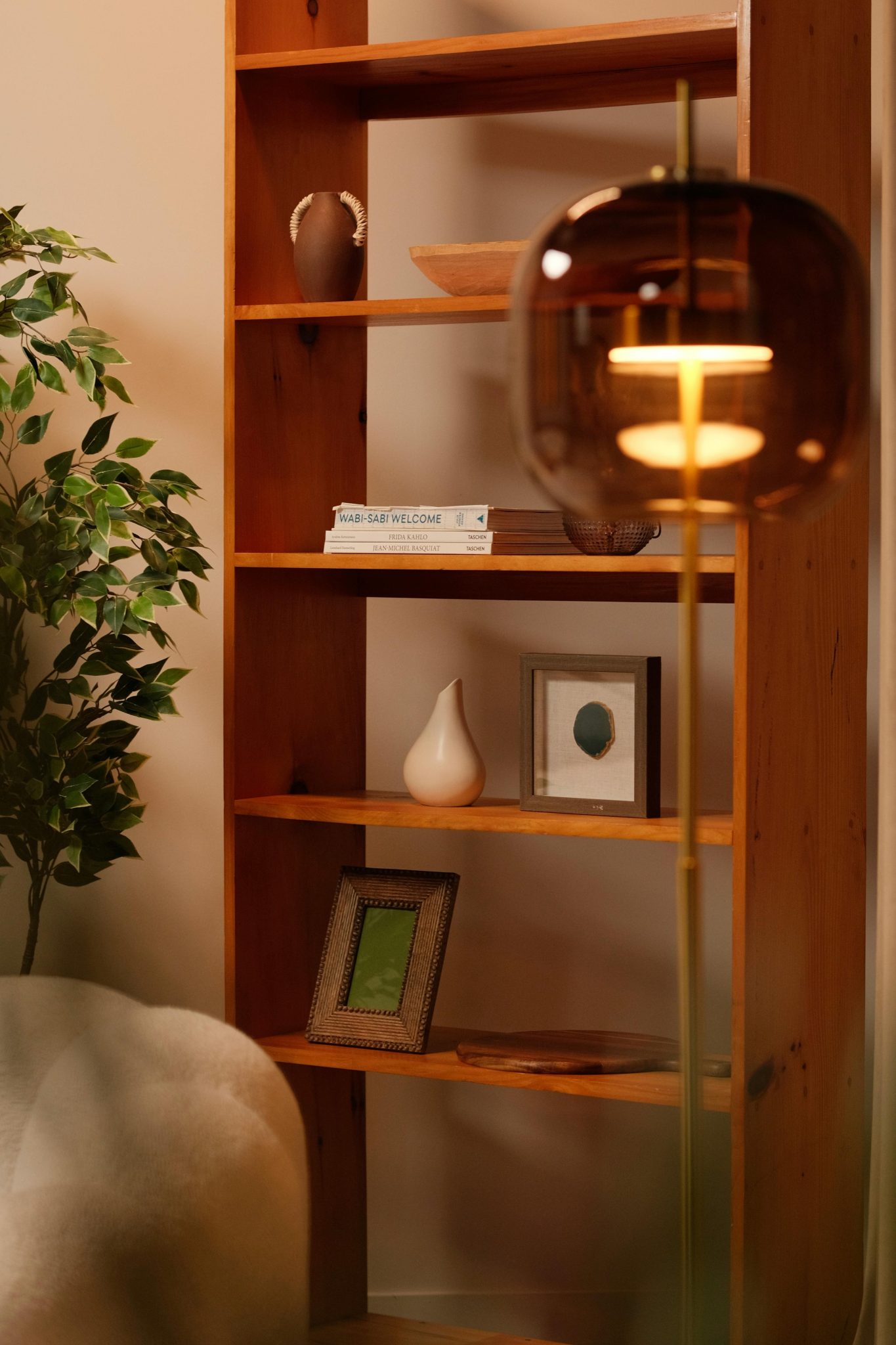 Warm minimalist living room featuring a wooden bookshelf and floor lamp.