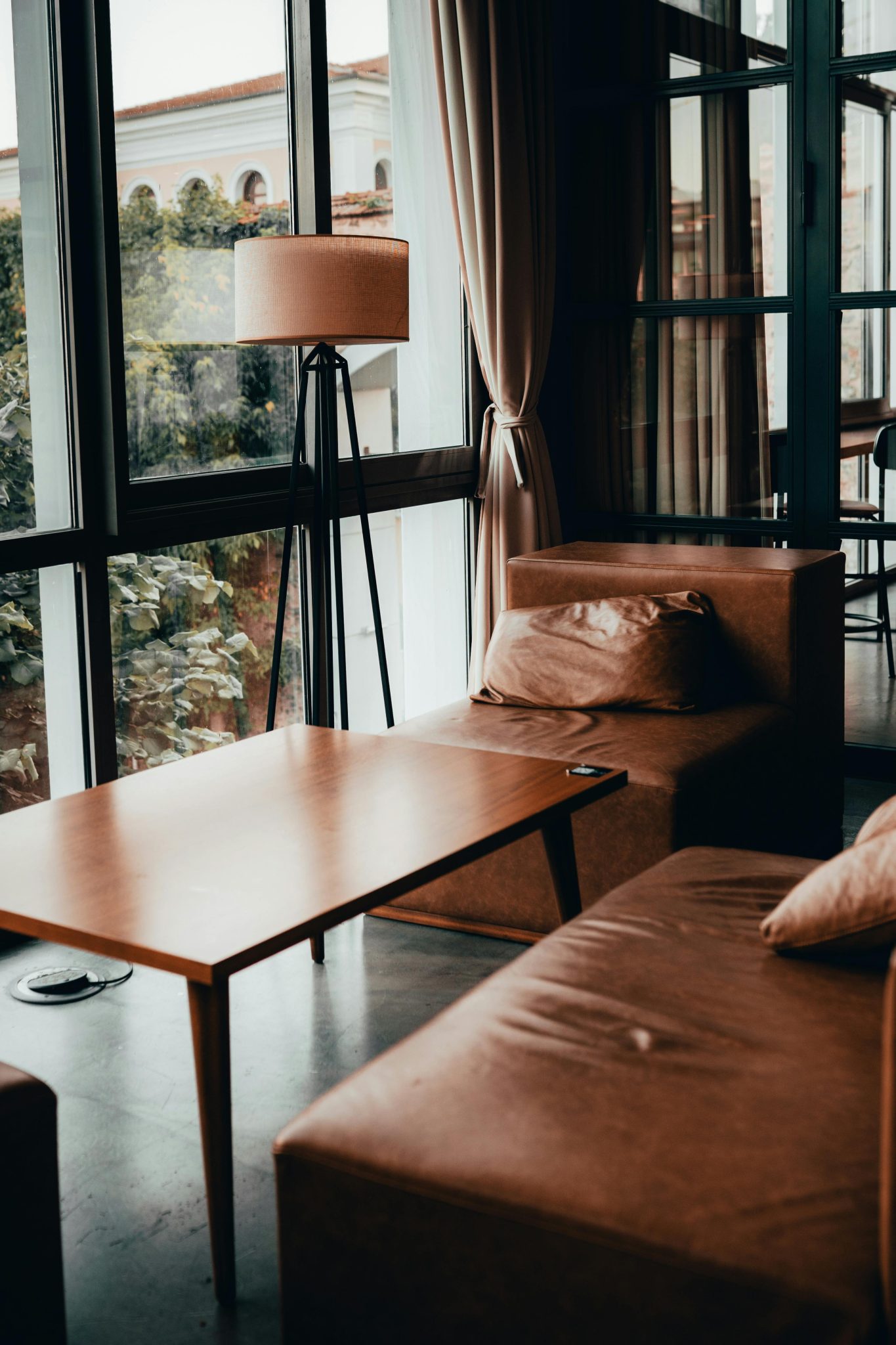 Warm-toned modern lounge with brown couches and natural light through large windows.