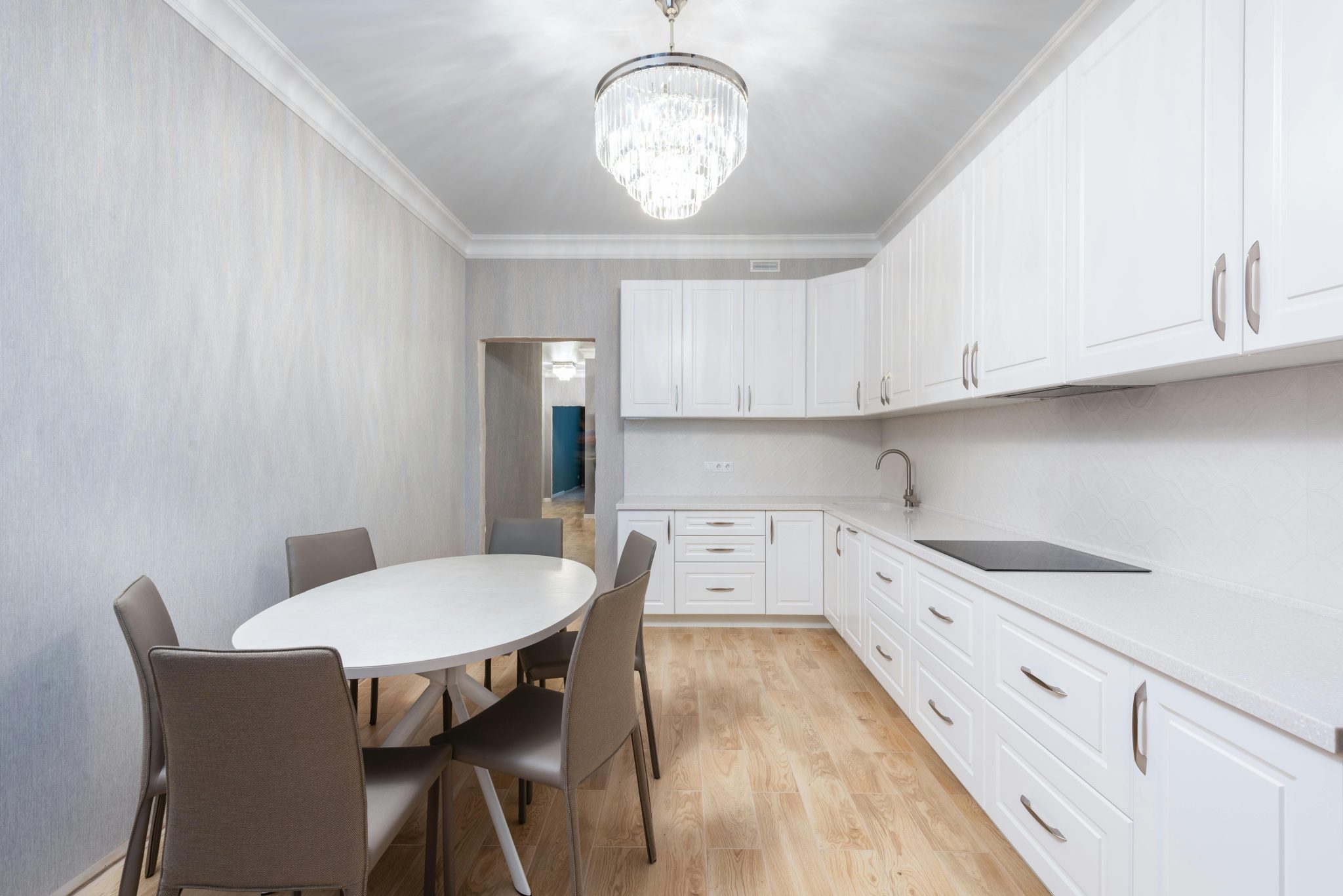 White cabinets and built in stove against oval shaped table with chairs illuminated by chandelier at home