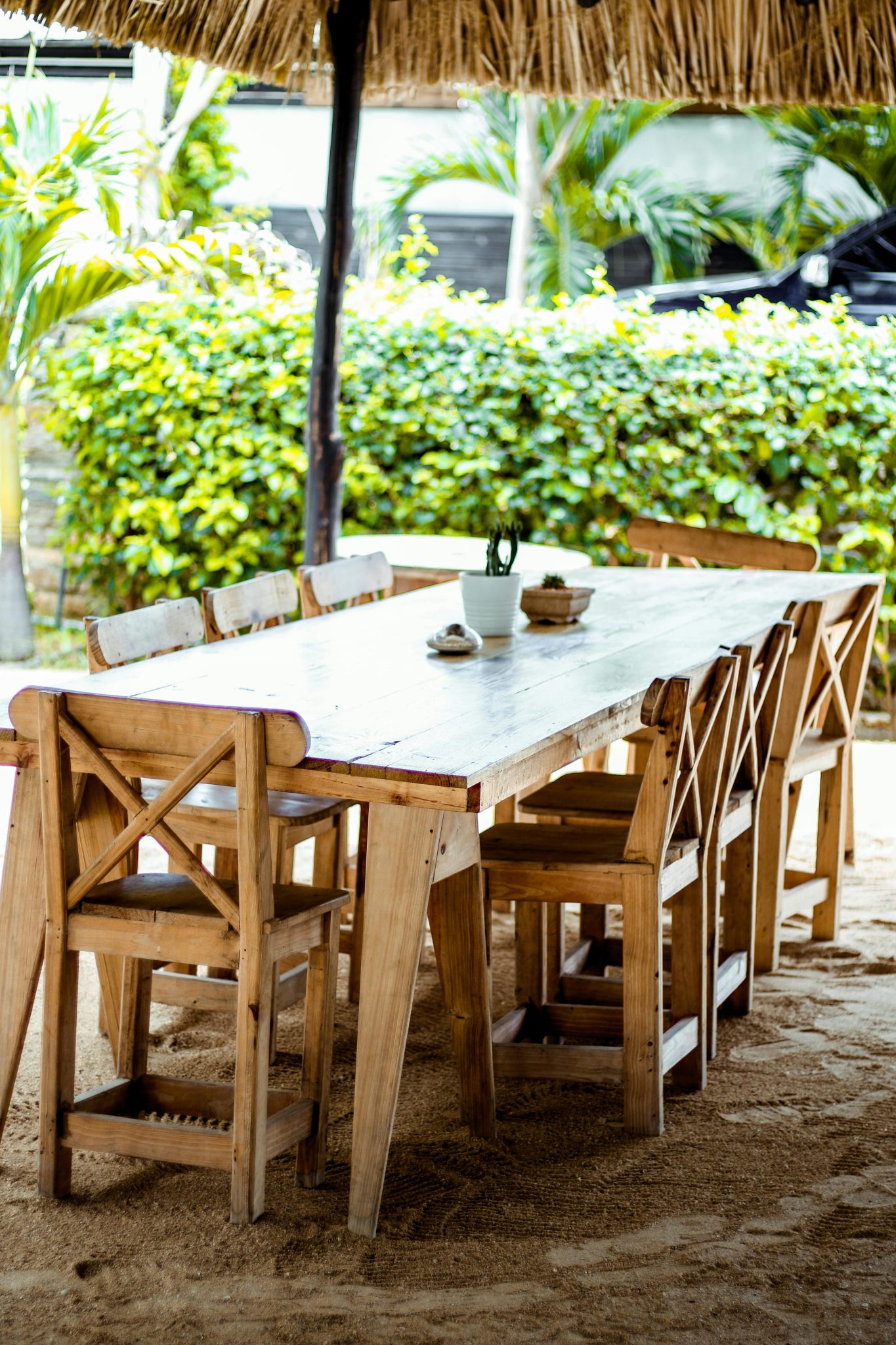 Wooden table and chairs under a thatched roof in a lush outdoor setting.