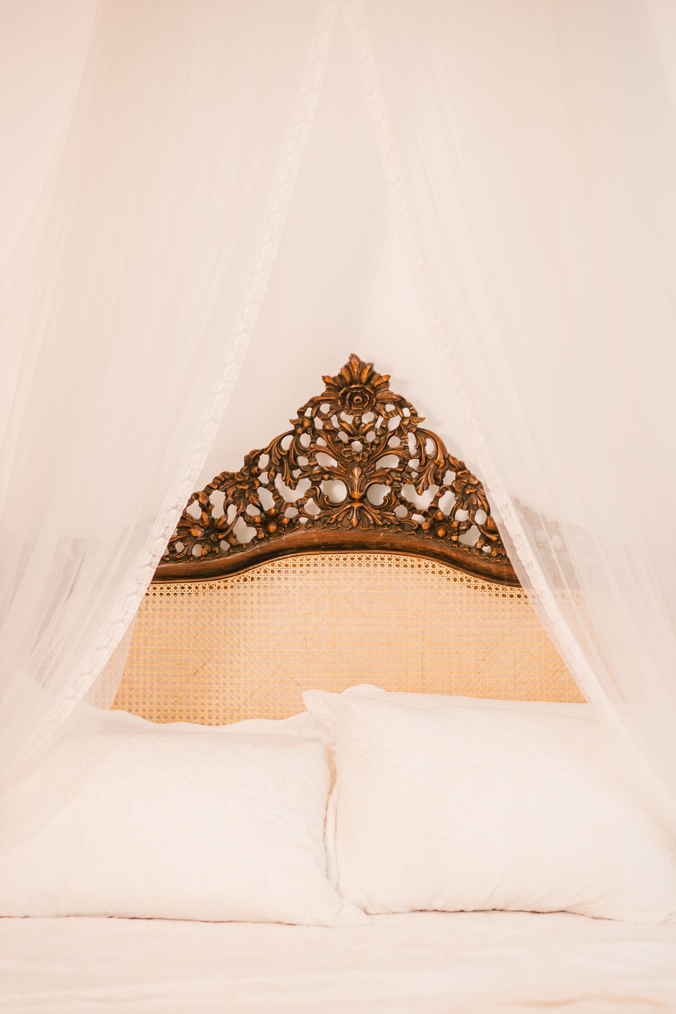 A beautifully elegant canopy bed featuring an intricately carved wooden headboard and soft white pillows.