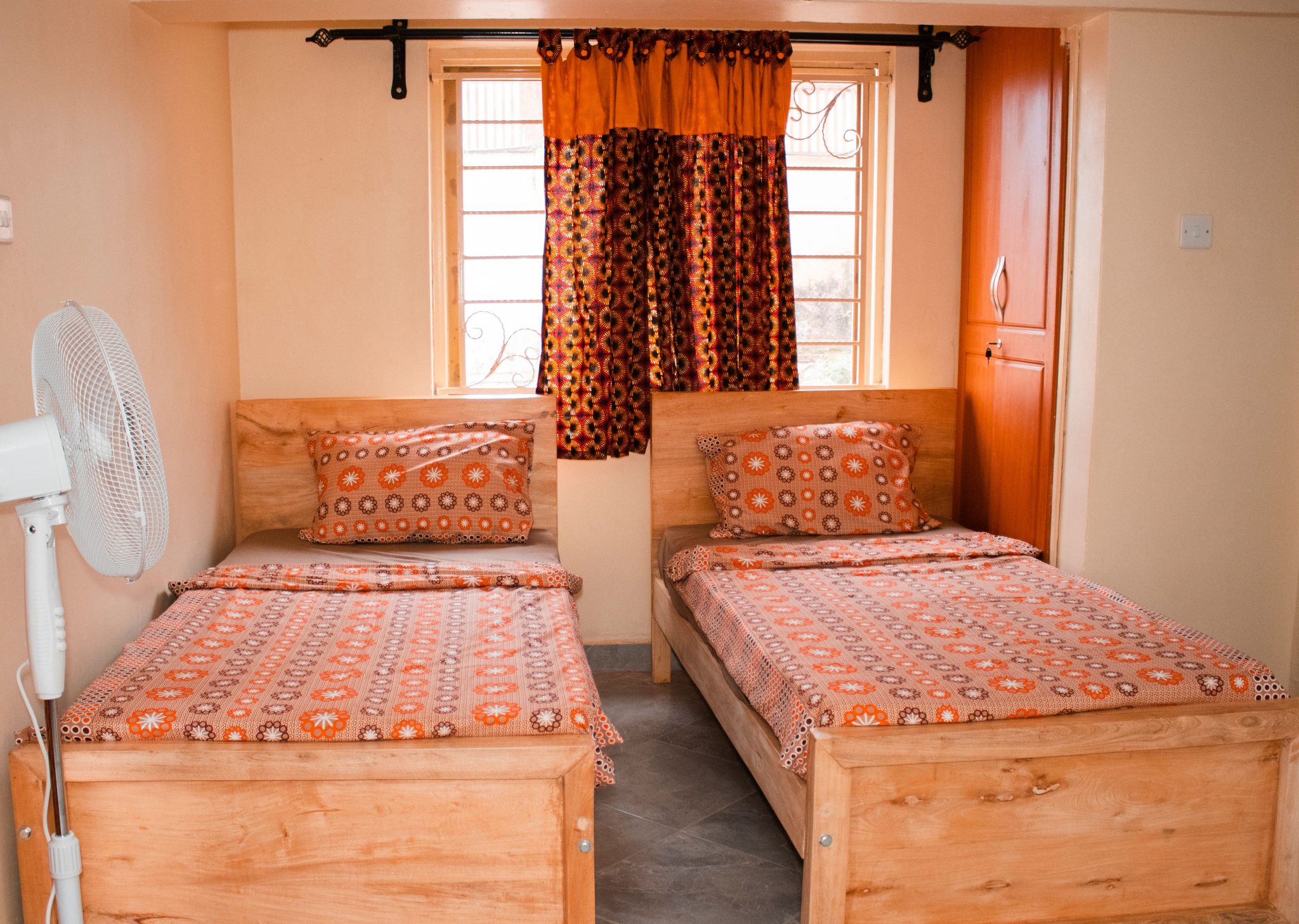 A brightly lit twin bedroom in Kampala, Uganda, featuring matching patterned bedding and wooden furniture.