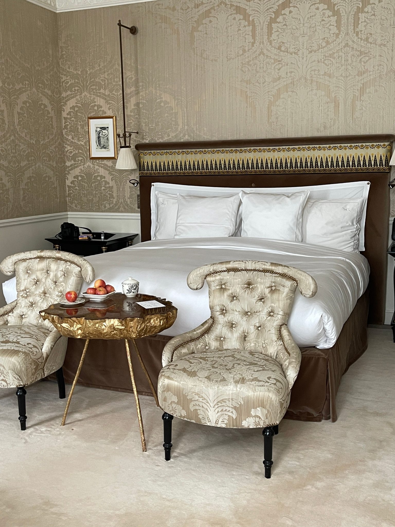 A luxurious hotel bedroom featuring classic decor with armchairs and a plush bed.