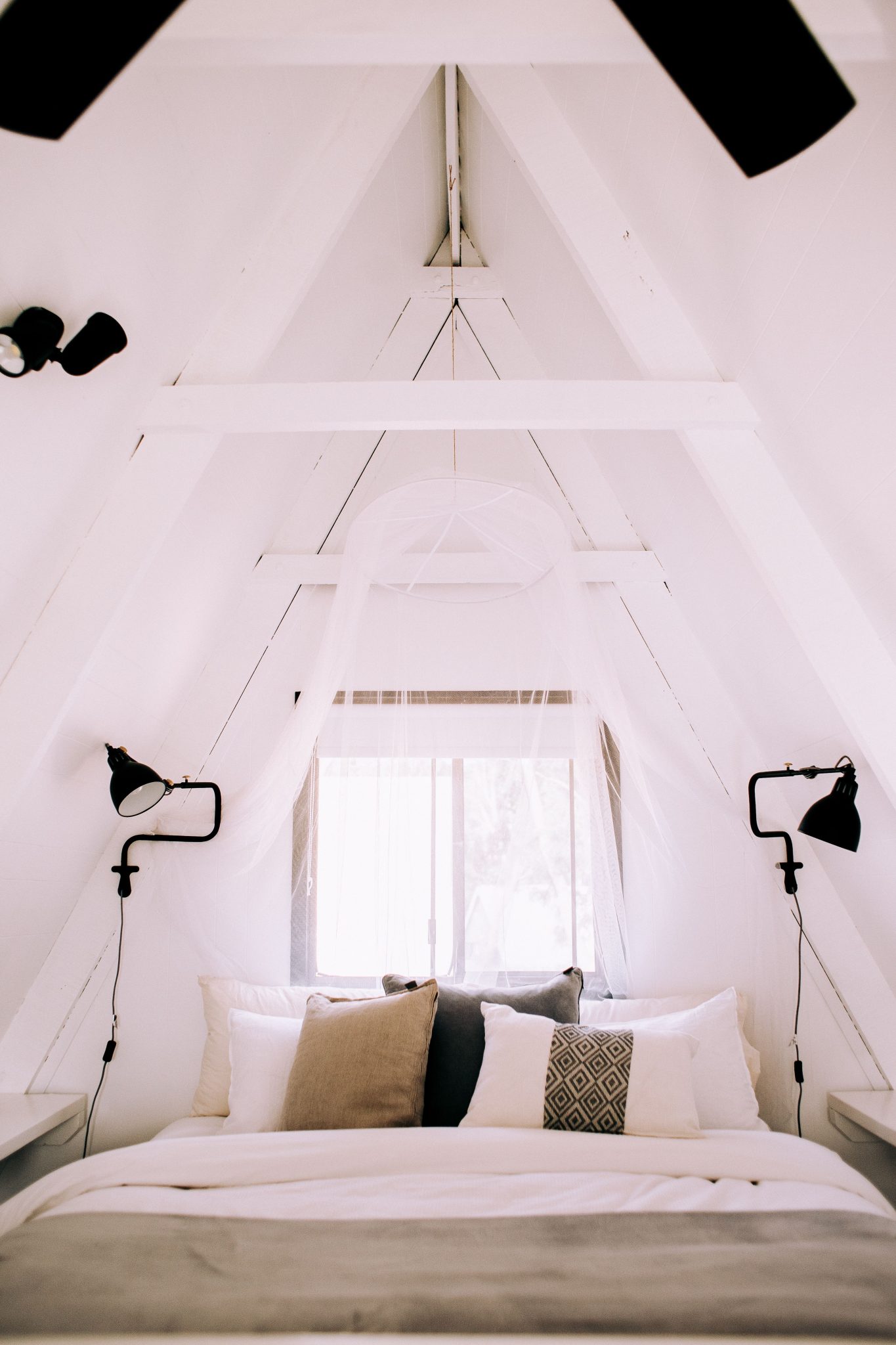 A minimalist A-frame attic bedroom featuring a cozy white bed with natural light.