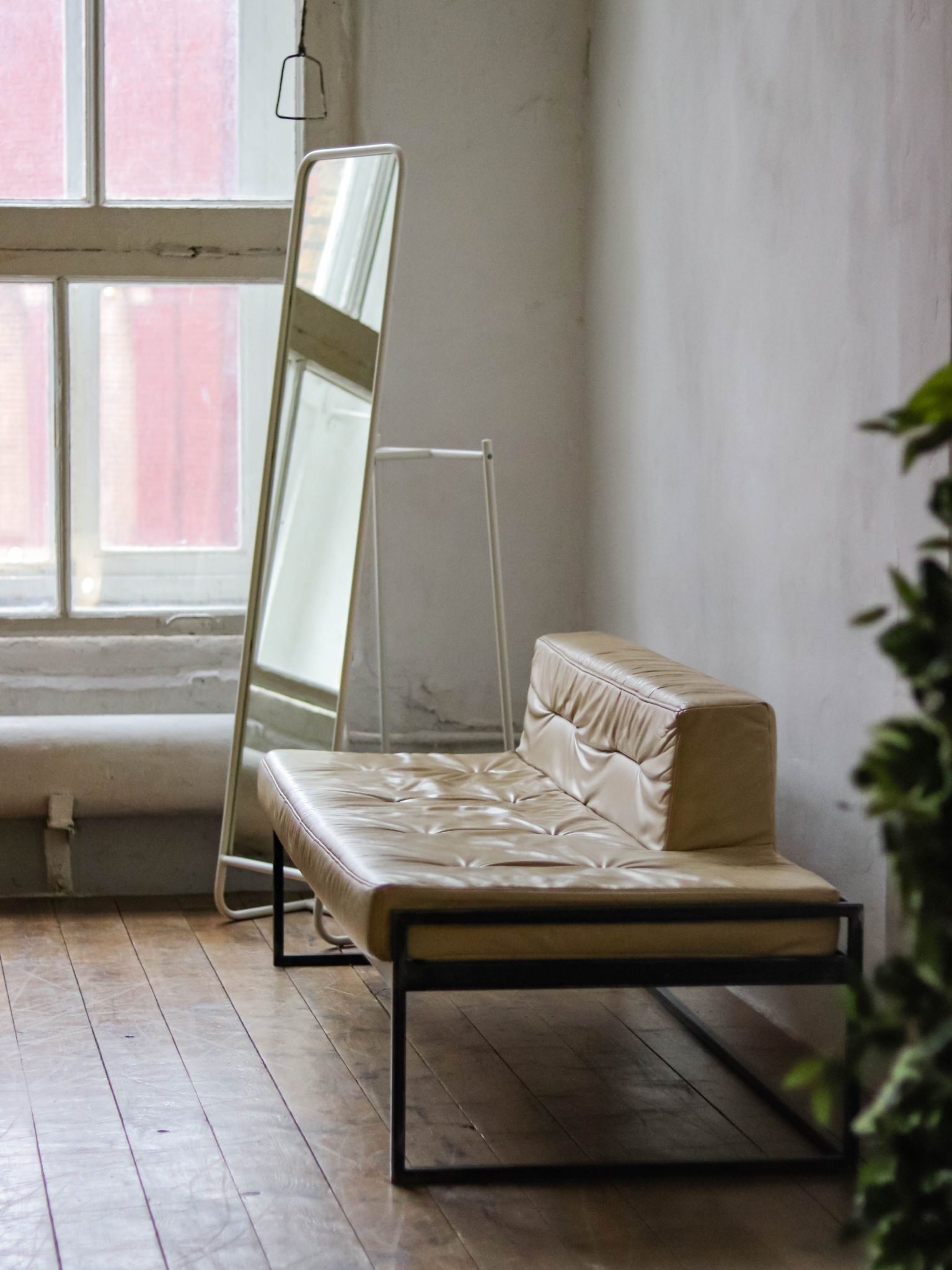 A minimalist room featuring a leather chair and full-length mirror against a textured wall.