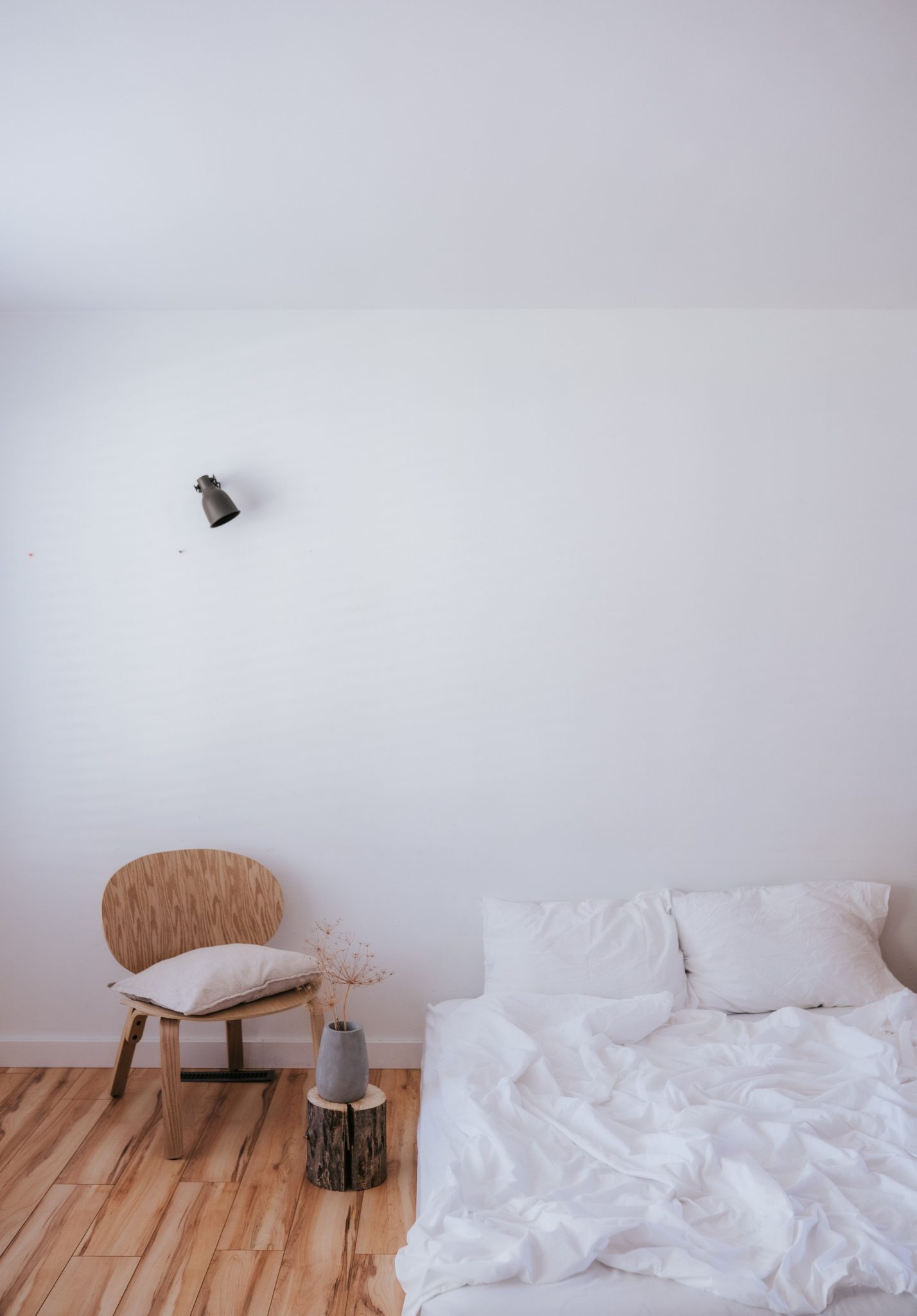 A minimalist Scandinavian-style bedroom interior featuring a white bed and wooden chair.