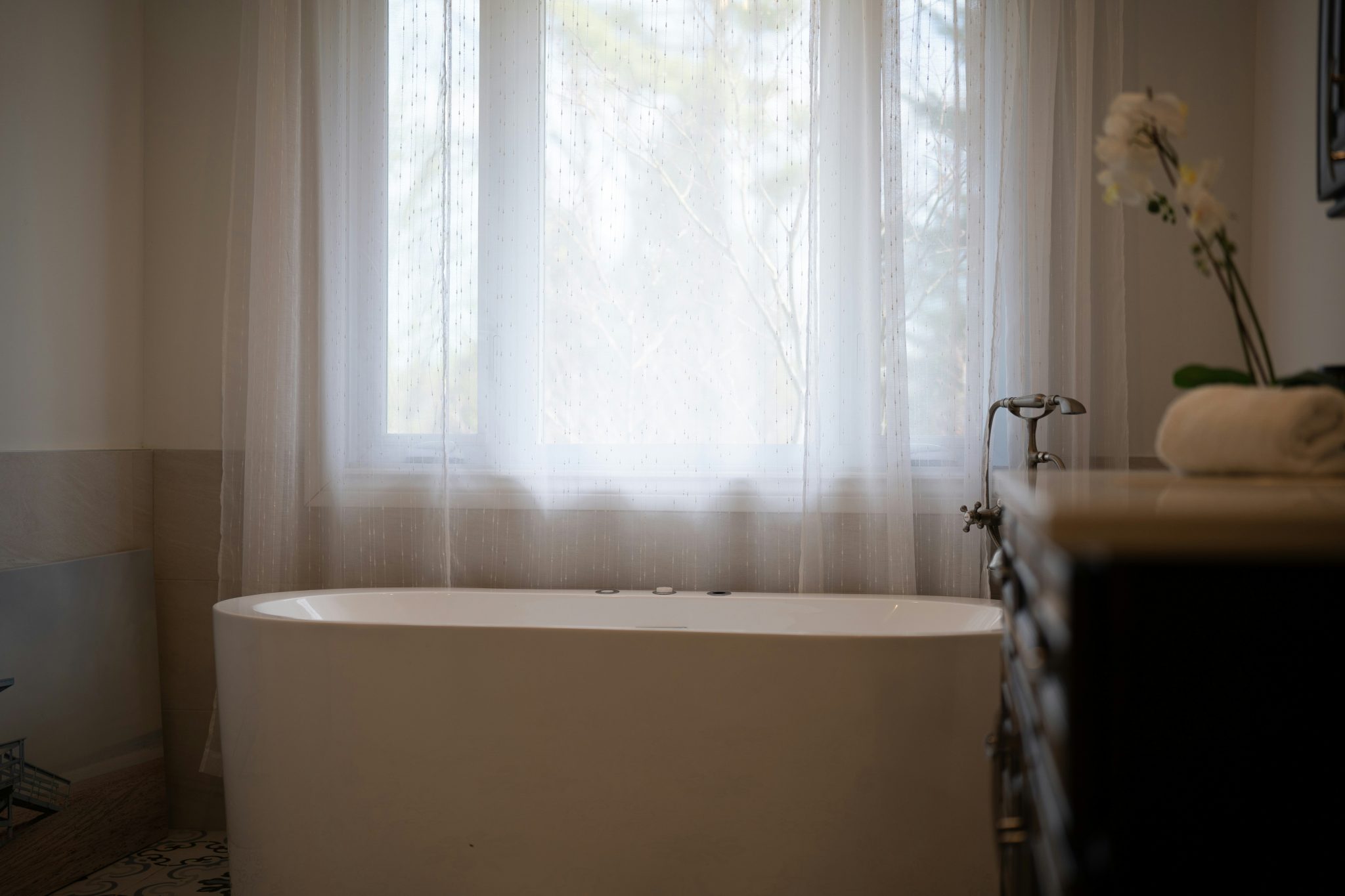 A modern bathtub with sheer curtains and a flower.