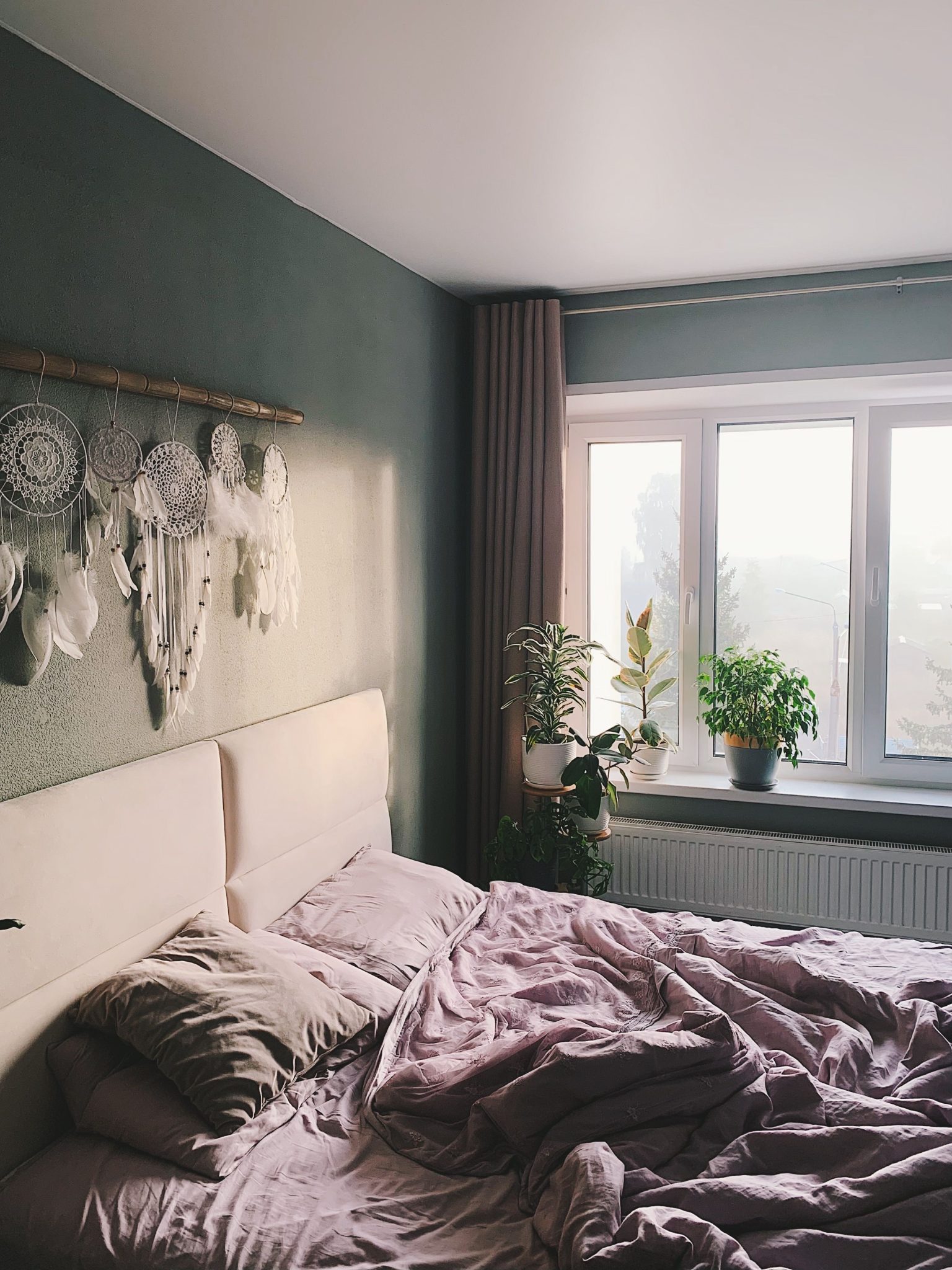 A modern, cozy bedroom featuring dreamcatchers and indoor plants.
