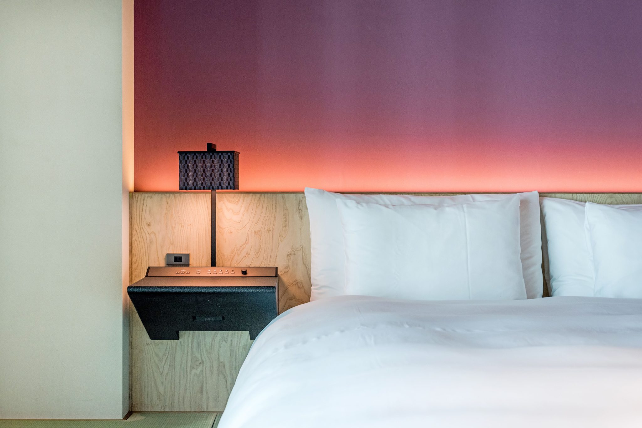 A modern, minimalist hotel room with elegant lighting and comfortable bed linen.