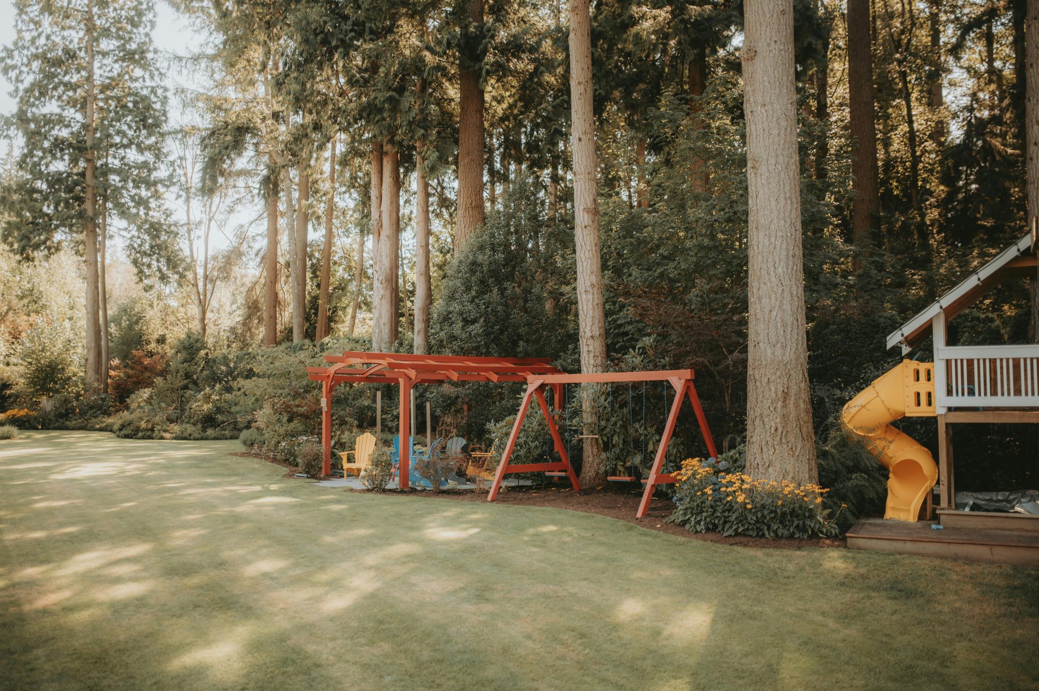 A peaceful outdoor playground with swings and slide amidst lush green forest setting, perfect for children.
