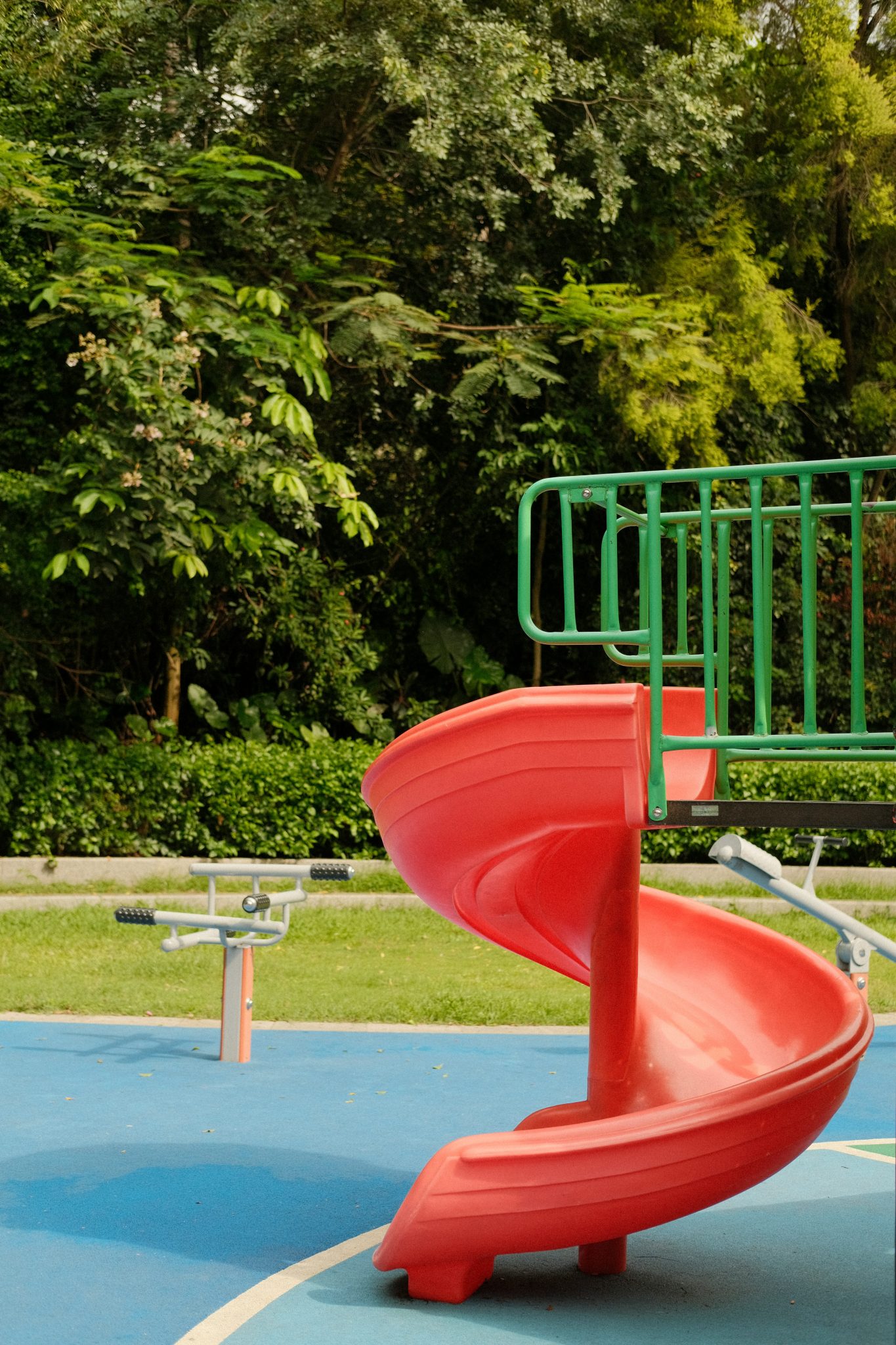 a playground with a red slide and green trees in the background