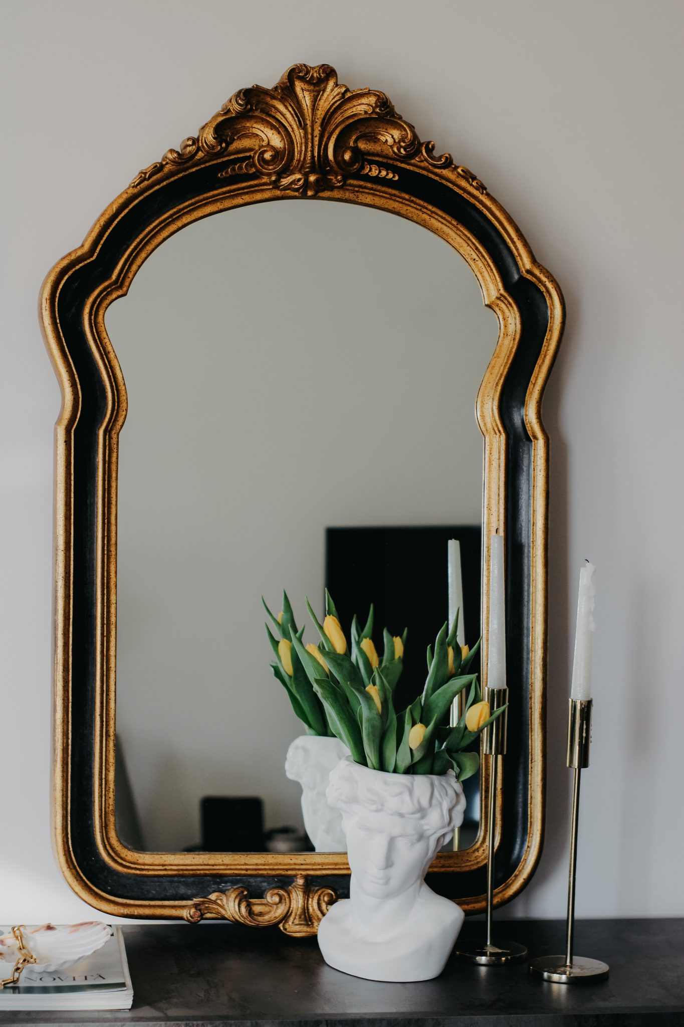 A sophisticated interior featuring an ornate mirror, a bust vase with tulips, and elegant candles.
