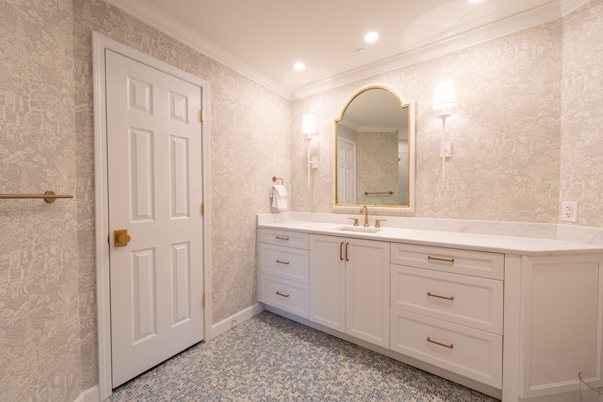 A spacious modern bathroom featuring a marble vanity, elegant lighting, and intricate wallpaper.