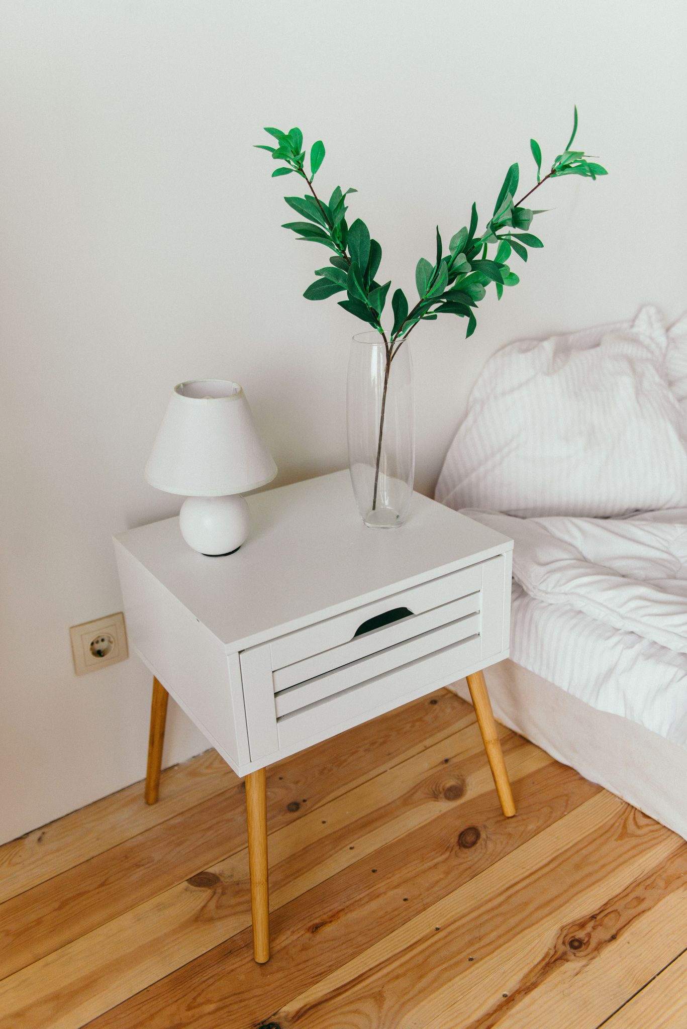 A stylish bedroom showcasing a white nightstand with a vase and lamp, perfect for modern interior design inspiration.
