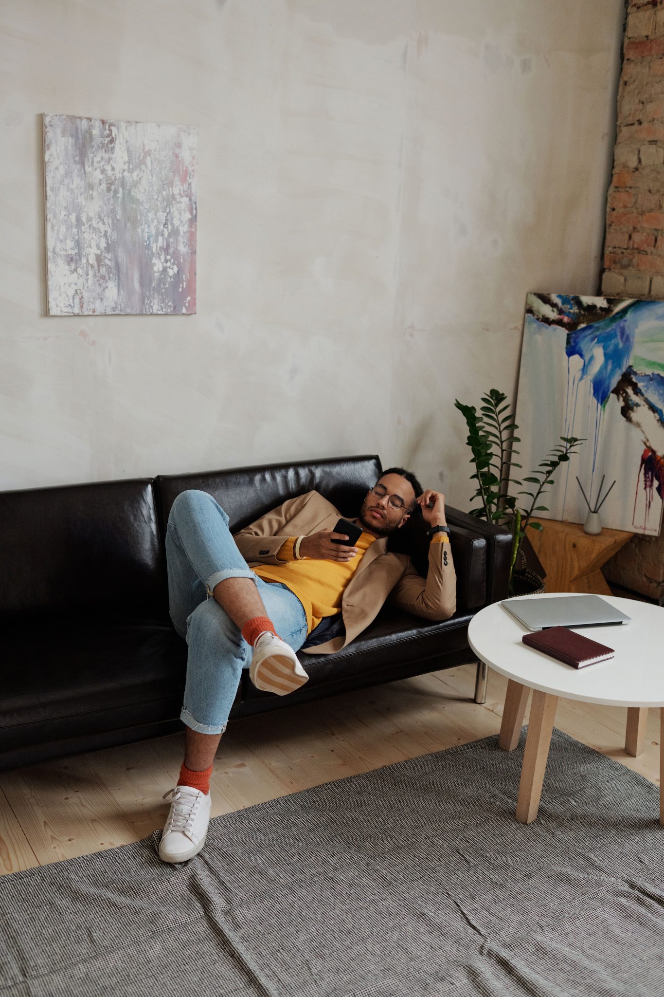 A stylish man relaxes on a leather sofa in a contemporary room with art and plants.